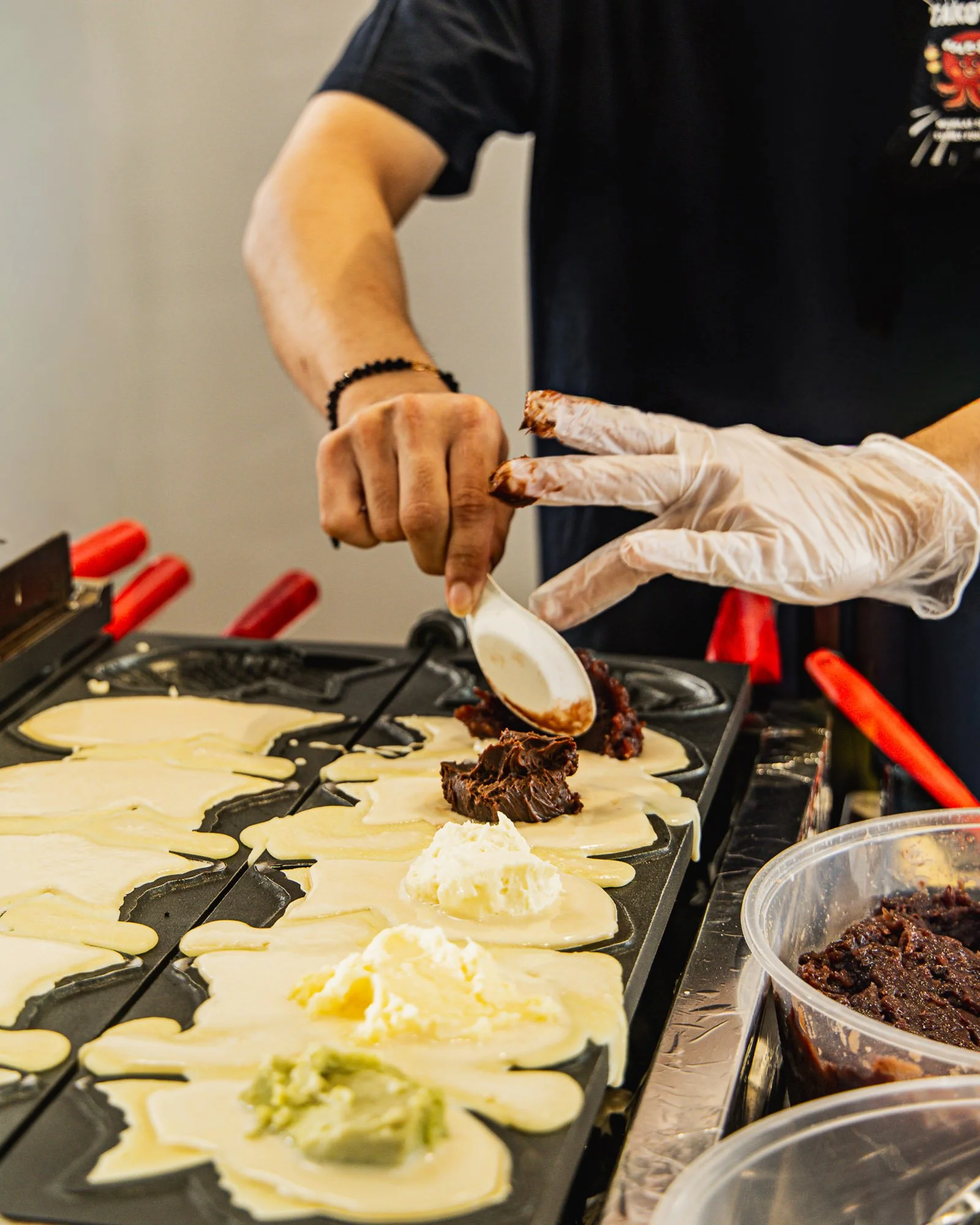 A person wearing black shirt and gloves preparing to eat crepes topped with chocolate and toppings.