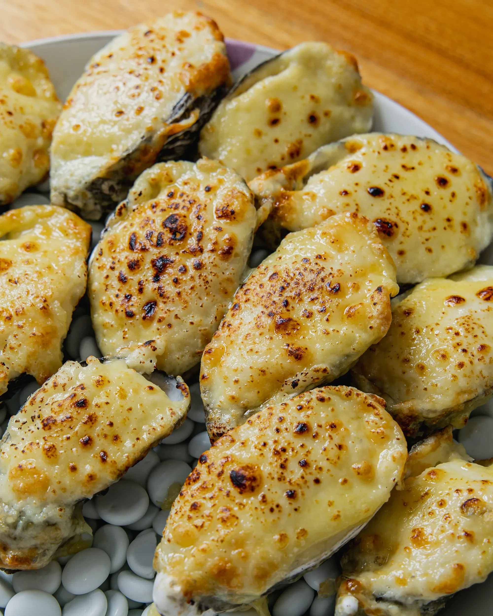 Close-up of baked oysters with melted cheese topping on a plate with white beans on a wooden table.