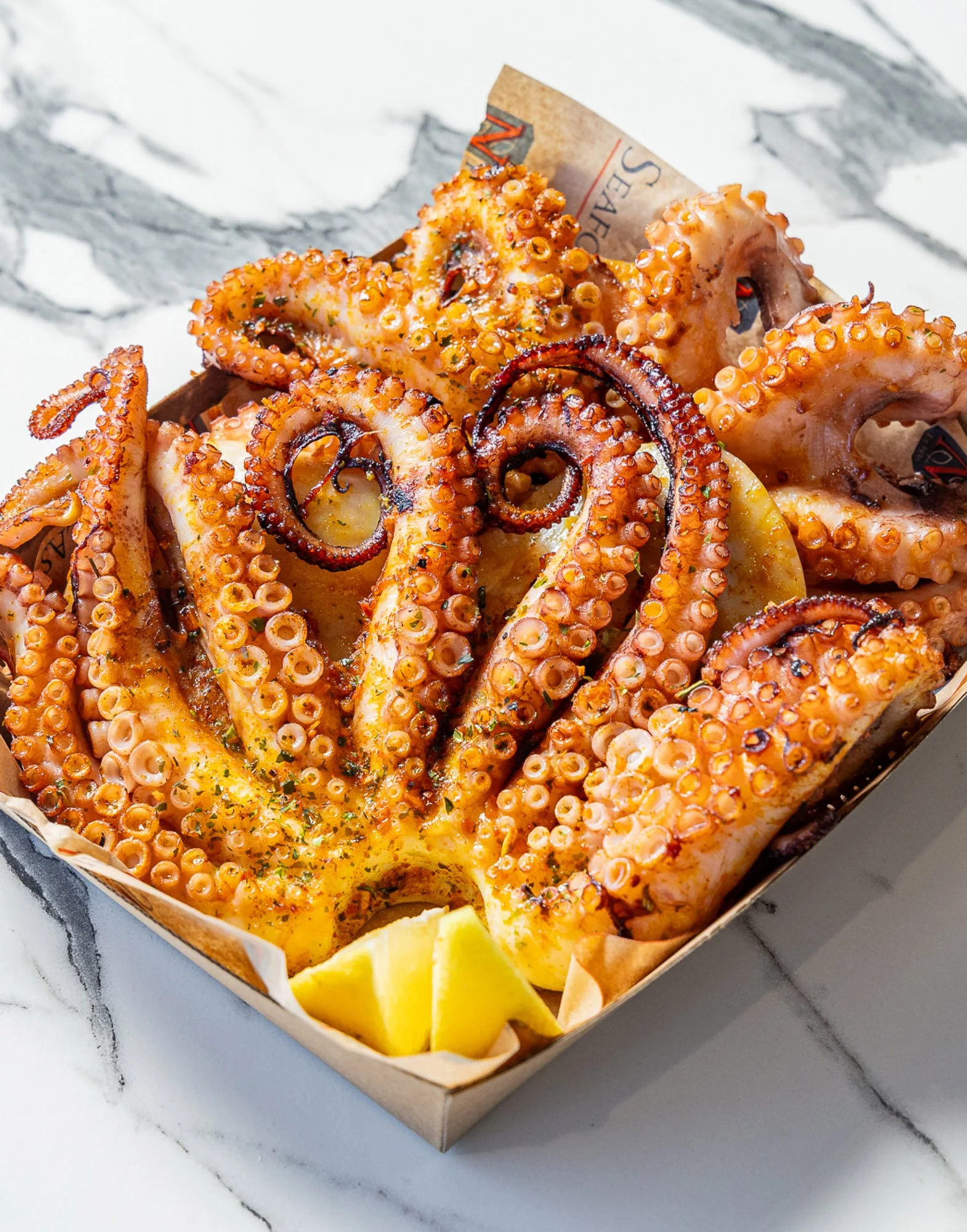 Close-up of cooked octopus tentacles served with lemon wedges on a white marble countertop.