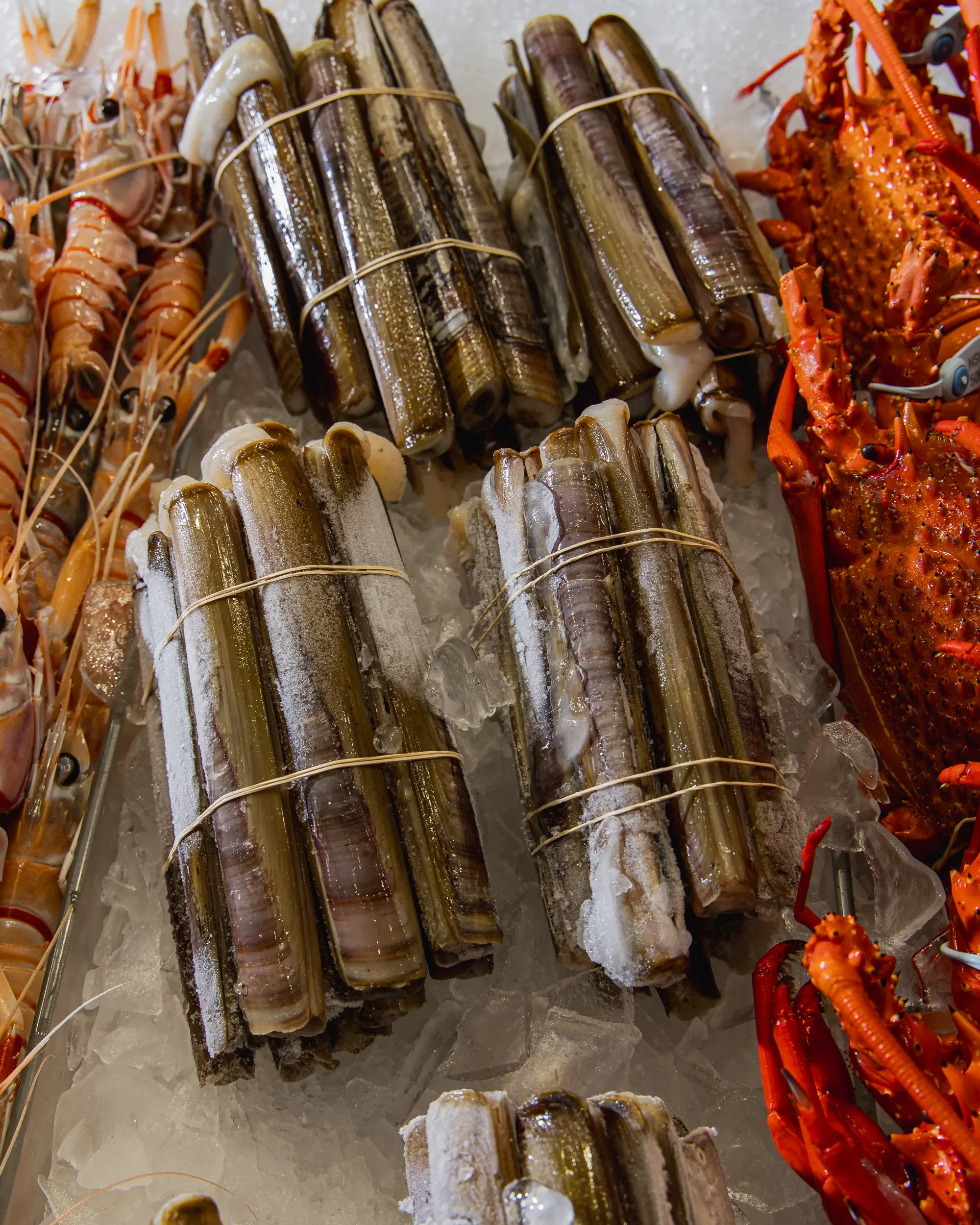 Bundled clusters of raw fish and lobsters on ice at a seafood market.