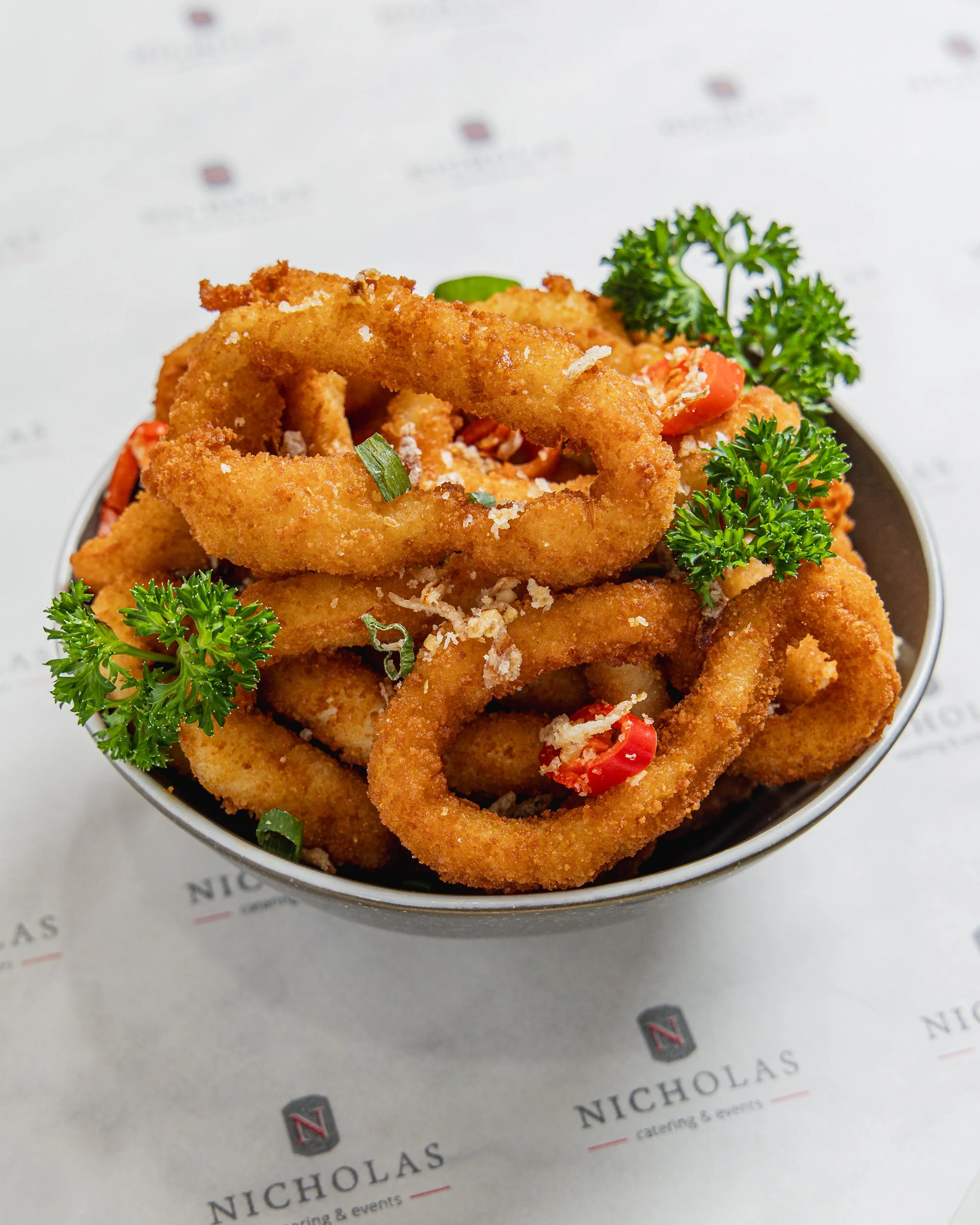 Close-up of fried onion rings garnished with parsley and chopped red pepper, served on a plate.