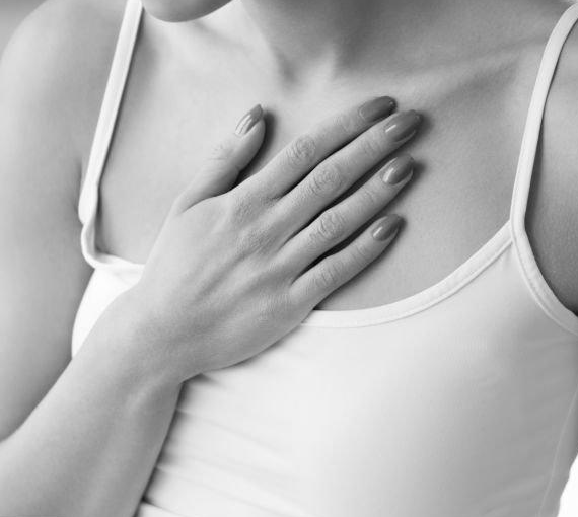 Black and white close-up of a woman wearing a white tank top, with her left hand placed over her chest.