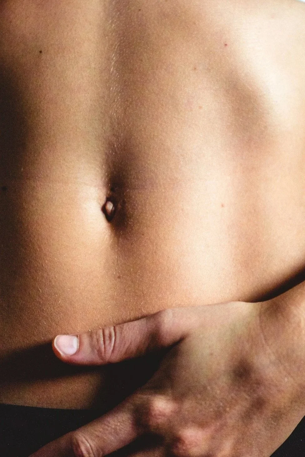 Close-up of a person's bare abdomen with a finger touching their lower stomach.
