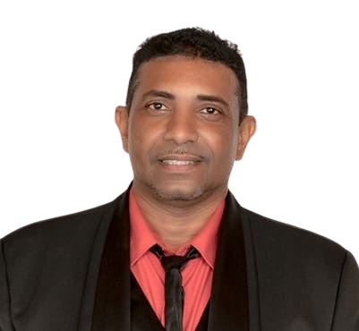 A man in a black suit, pink shirt, and black tie posing against a black background.