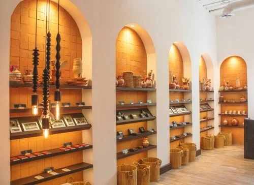 Interior of a store with arched shelves displaying various products, wicker baskets on the floor, warm lighting, and a wooden floor.