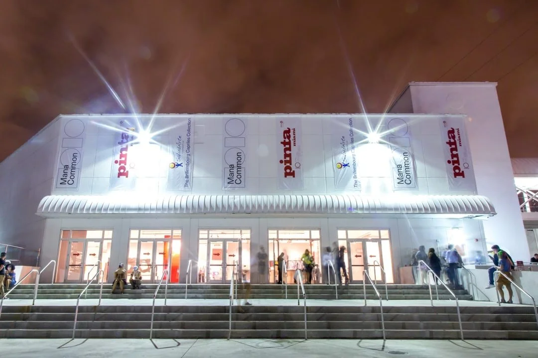 Night photo of a large public building with signs that say 'Mama Common' and 'Pinta.' There are stairs leading to multiple entrances, and people are walking and sitting outside.