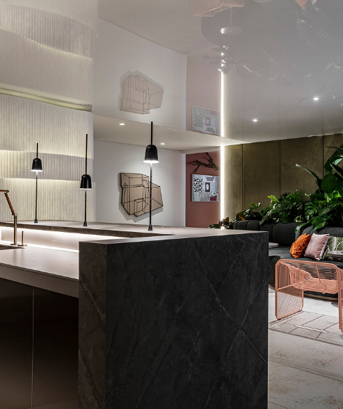 Modern interior with a kitchen counter, black pendant lights, wall-mounted art, and a cozy seating area with plants.