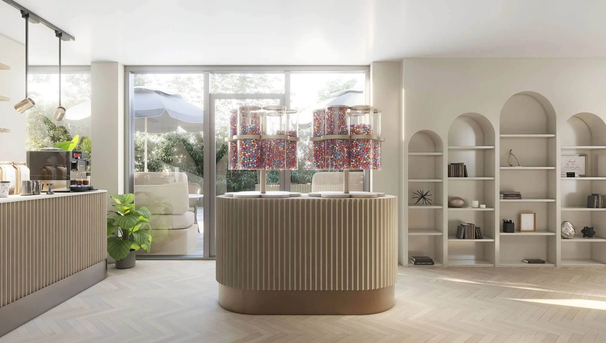 Modern interior with a coffee station, a display of large jars filled with colorful candies, white built-in shelves with decorative objects, and a large window with outdoor patio furniture and umbrellas.