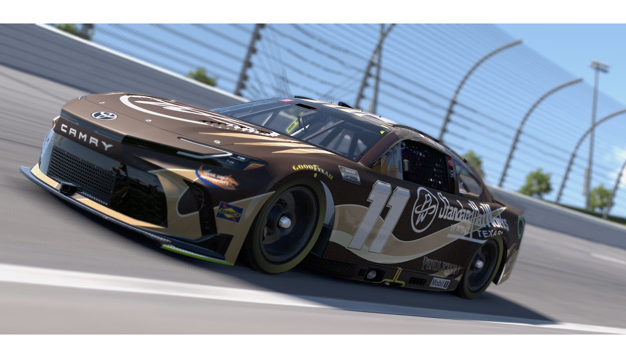 A race car on a racetrack with a large rear wing, racing decals, and the number 11 on its side, speeding past the safety barrier.