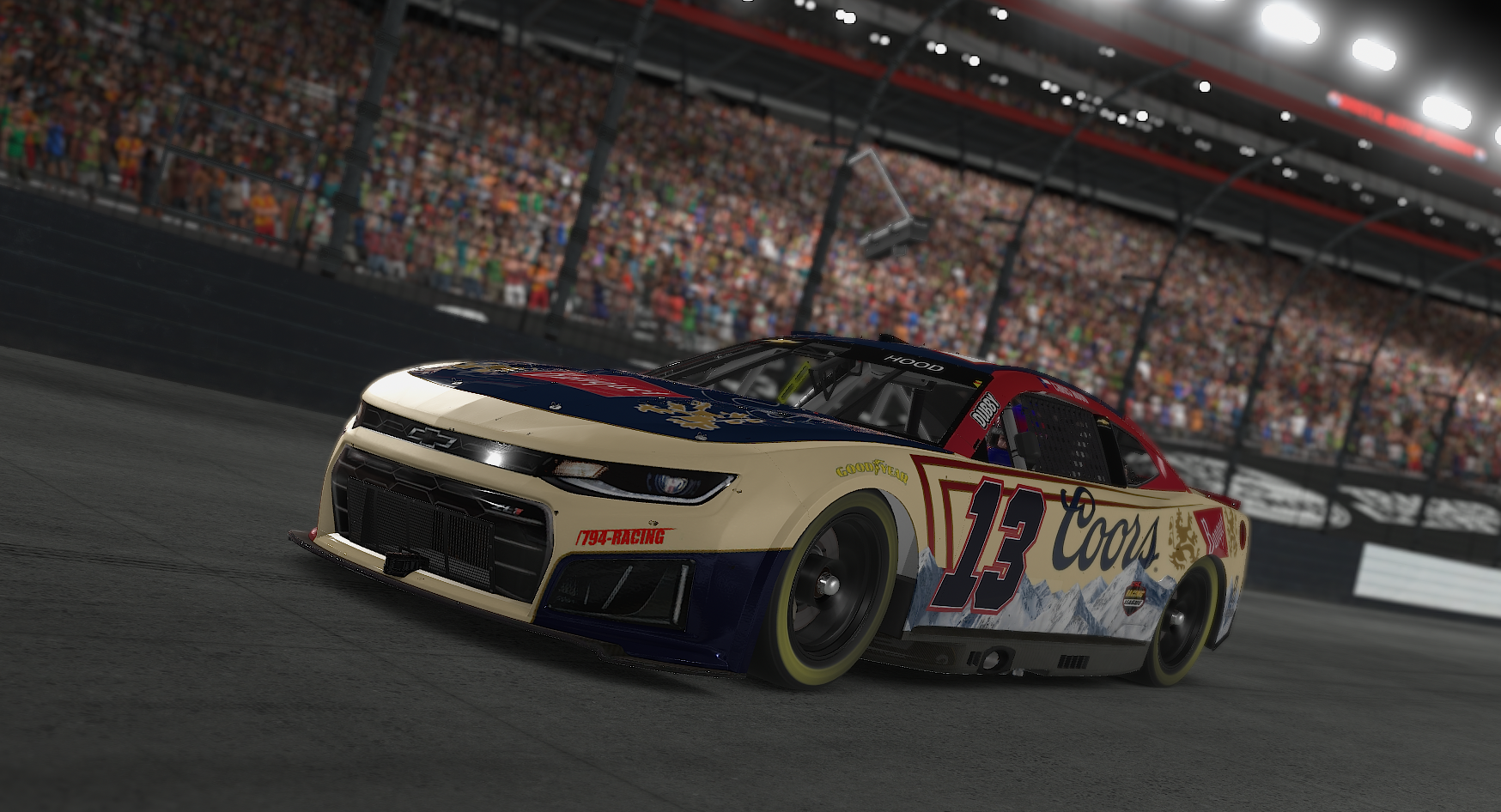 A race car on a racetrack, with a crowd in the stands behind it. The car has a cream, blue, and red paint scheme, featuring the number 13 and sponsor logos including Coors and Goodyear.