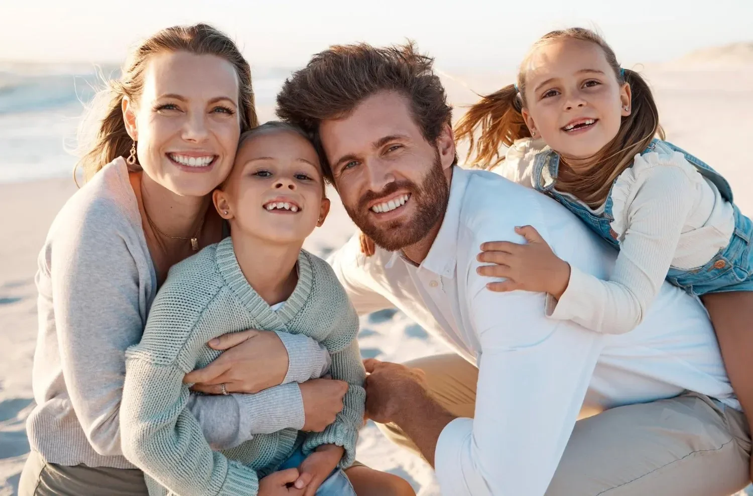 A happy family of five smiling on the beach, with two children, a man, and a woman all close together.