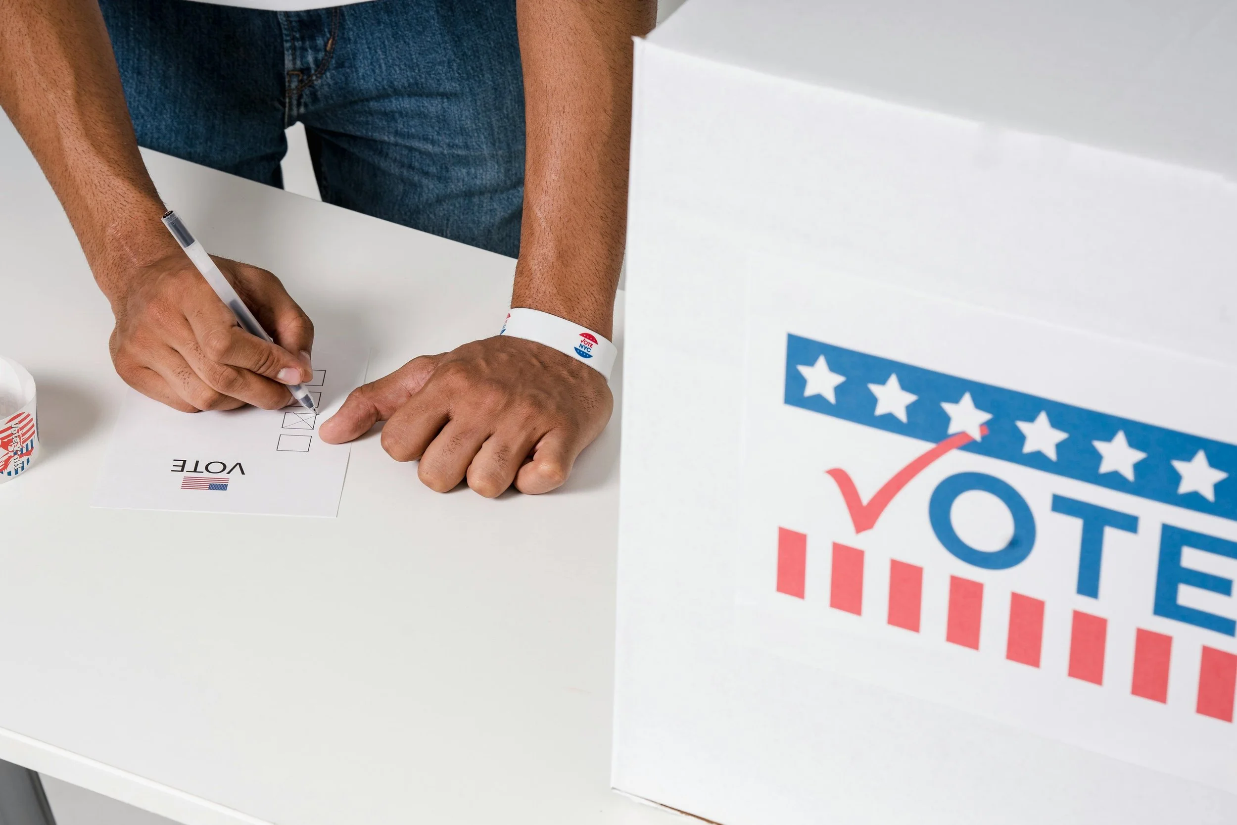 Person filling out a vote ballot at an election station, with a large 'Vote' ballot box nearby.