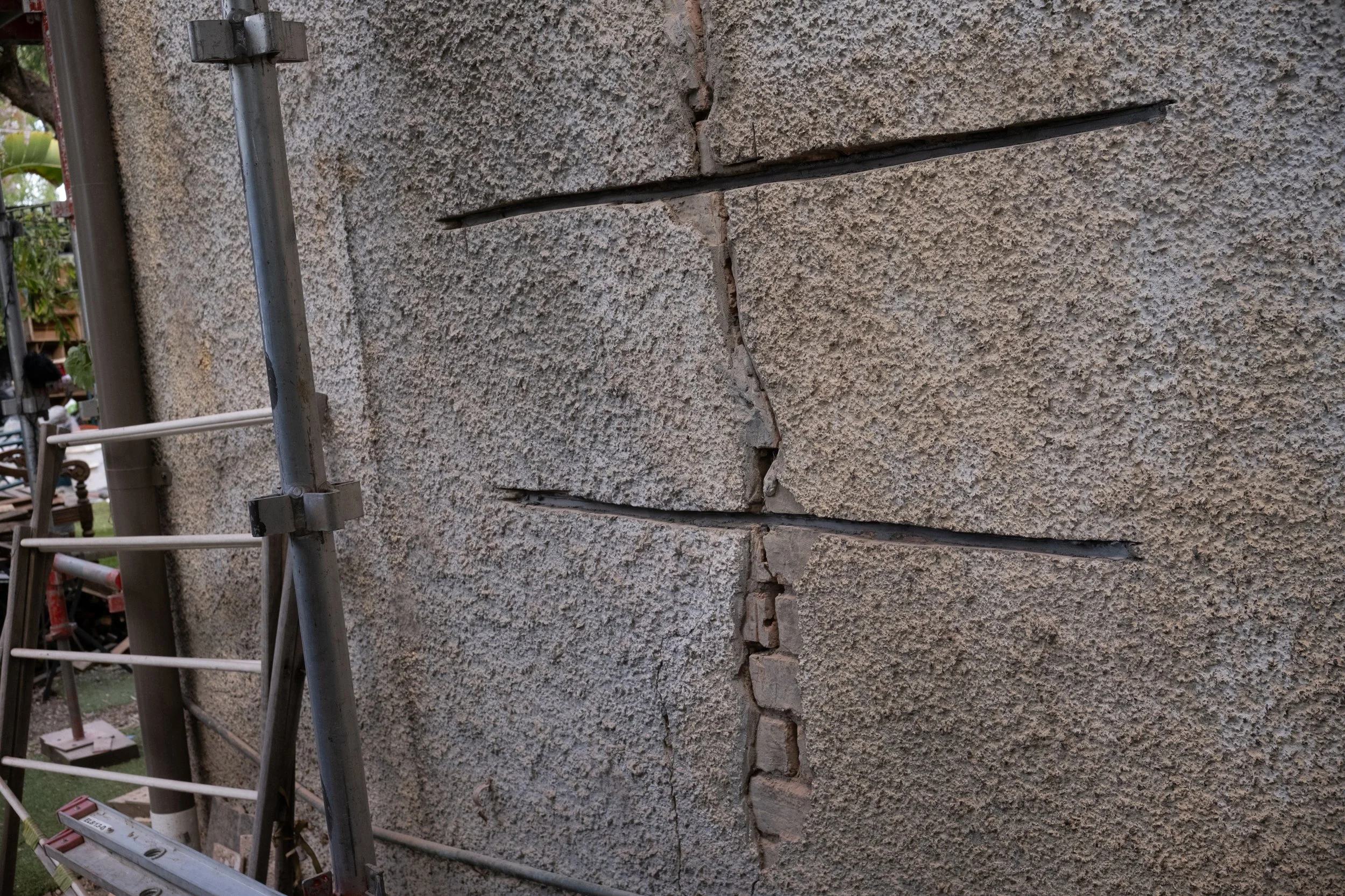 Close-up of a beige textured brick wall with a large vertical crack running through it, with some bricks displaced near the crack.