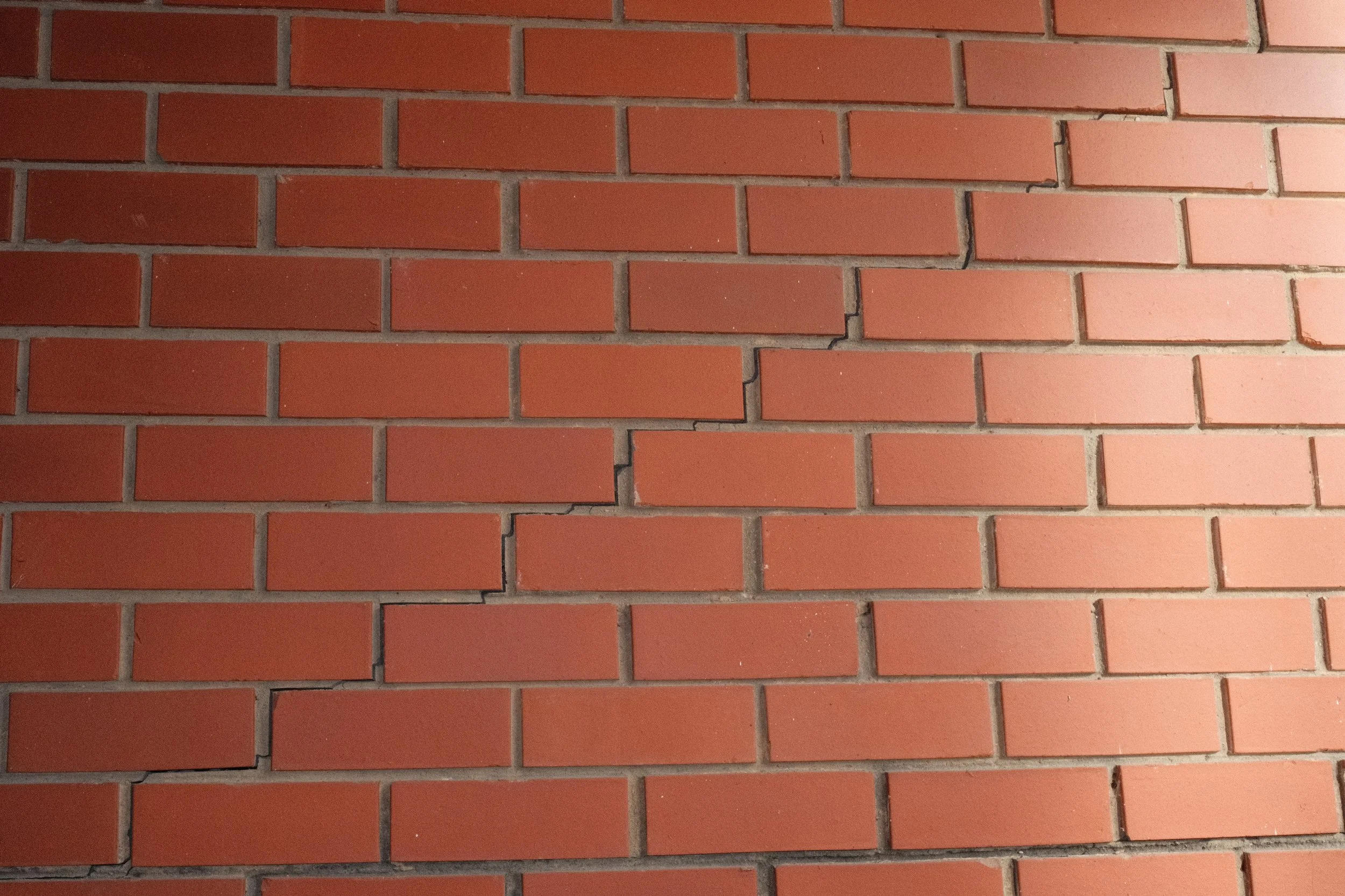 Close-up of a red brick wall with gray mortar joints, some bricks show cracks.