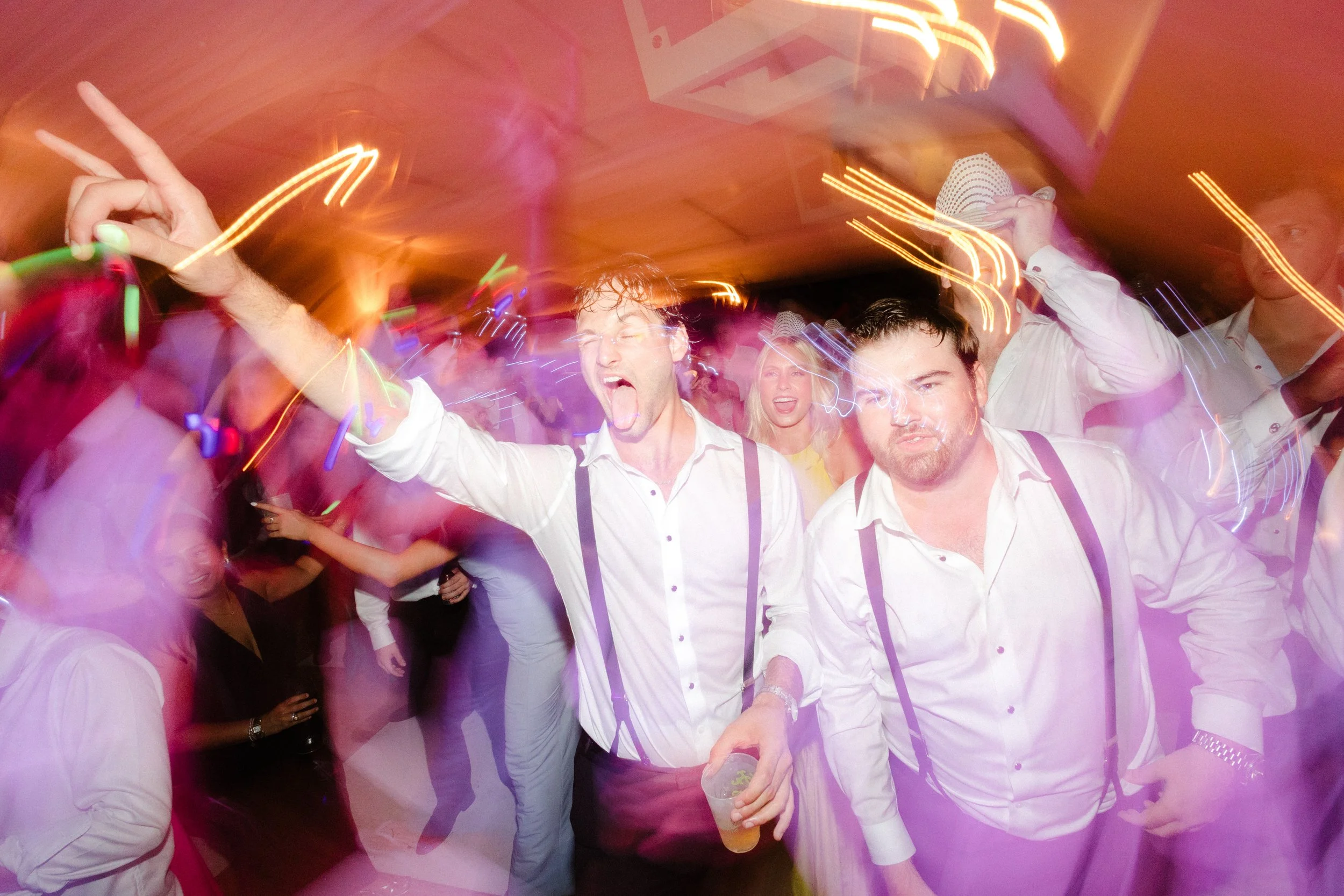 People dancing and enjoying at a party with colorful lights and motion blur, some holding drinks.