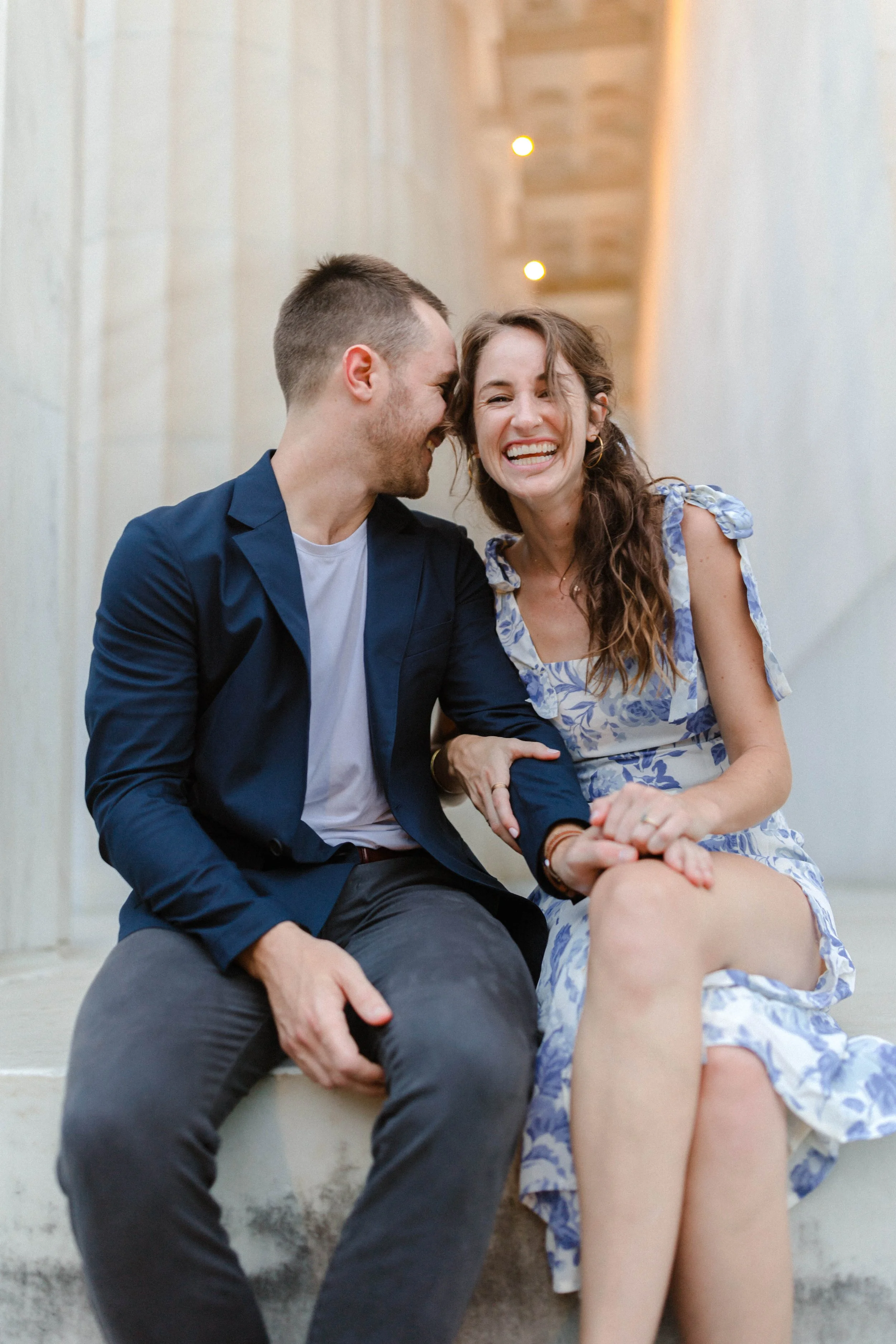 A young couple sitting on steps, smiling and laughing together, sharing a happy moment.