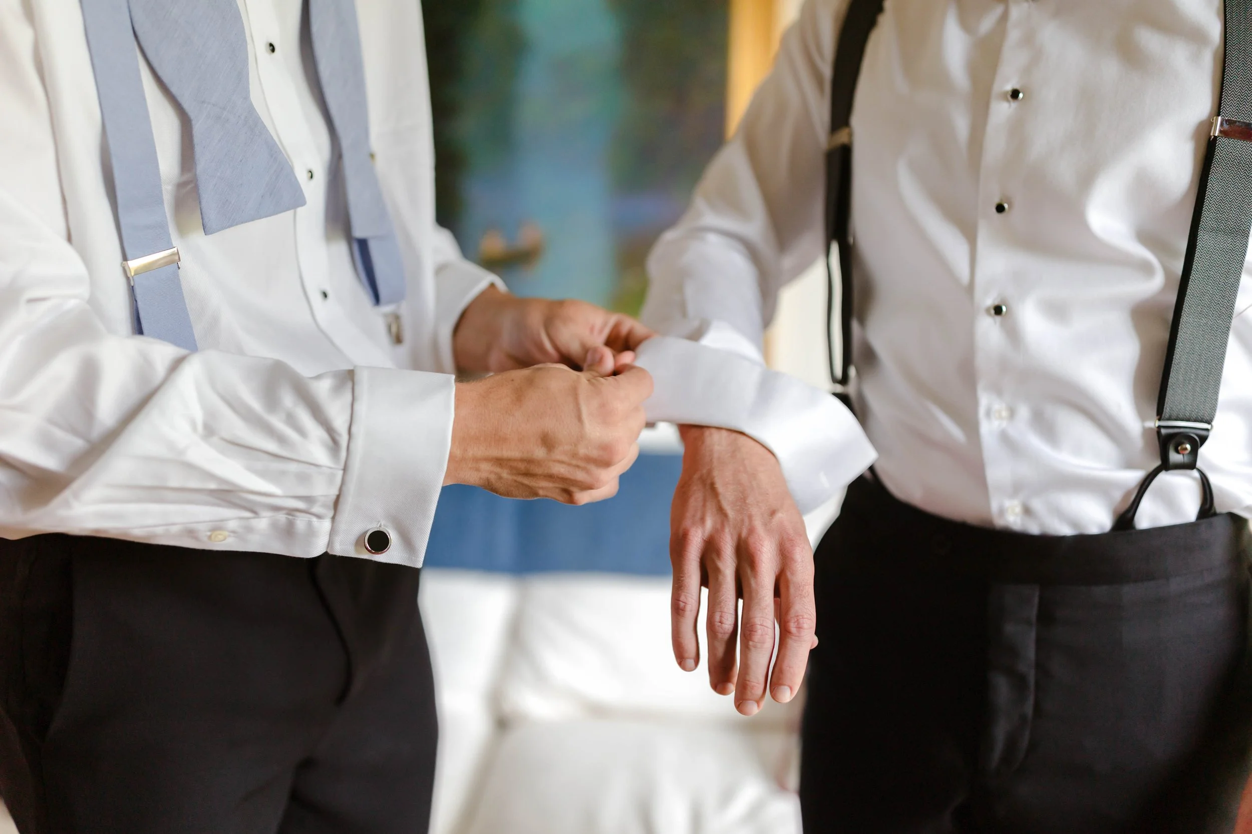 Two men in formal attire, one adjusting the other's shirt cuff. Wedding