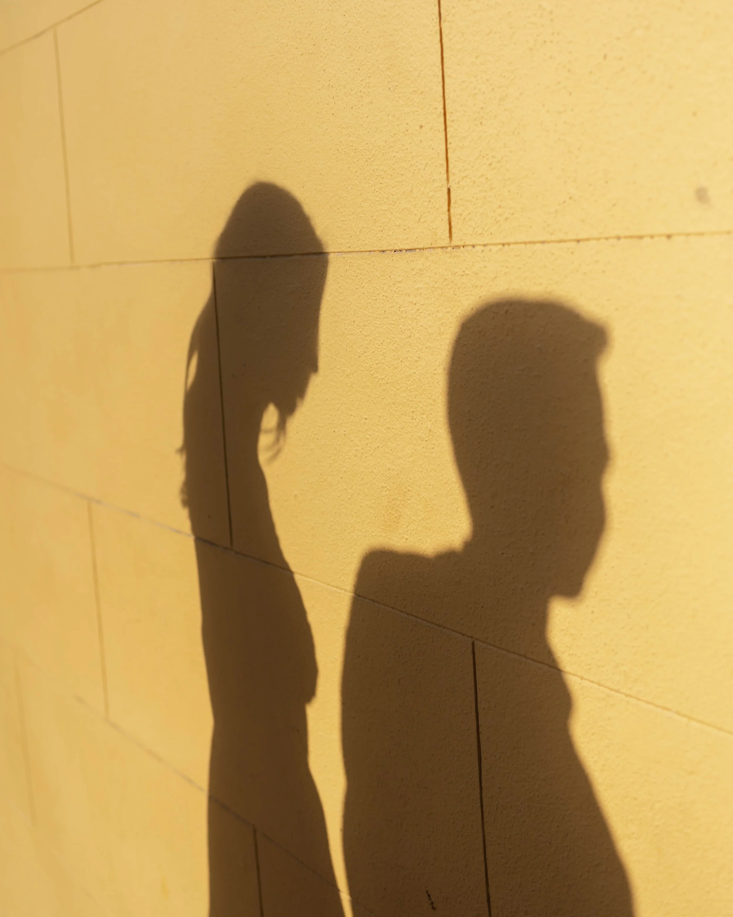 Shadow of a woman and a man on a yellow brick wall.