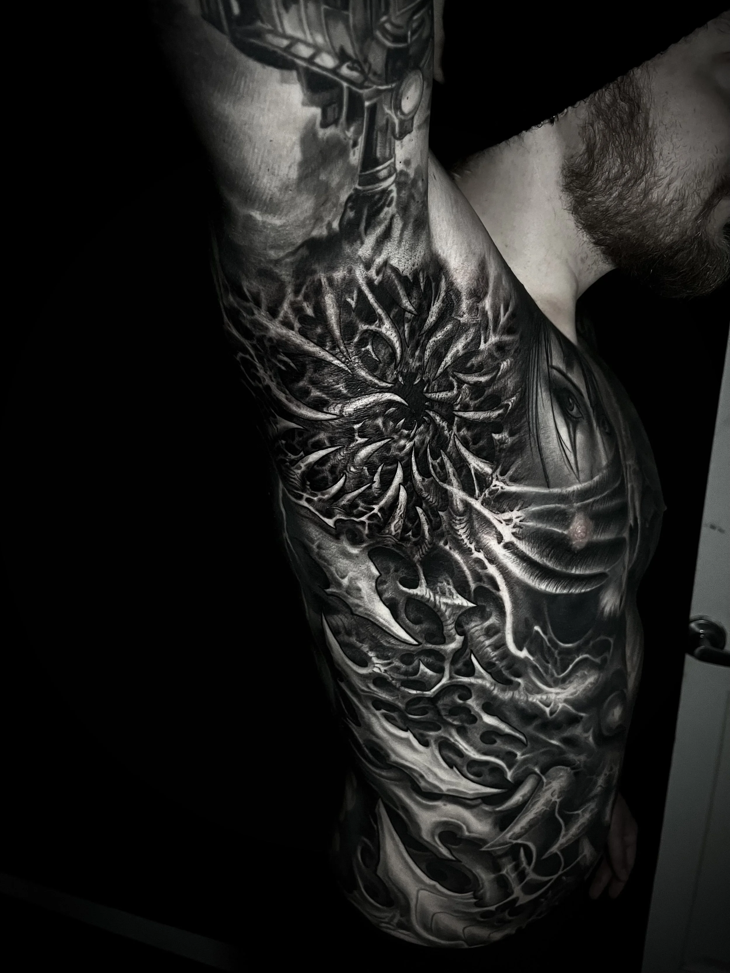 Black and grey tattoo sleeve on a person's upper arm and shoulder, featuring a dragon, a spiderweb pattern, and a woman's eye.