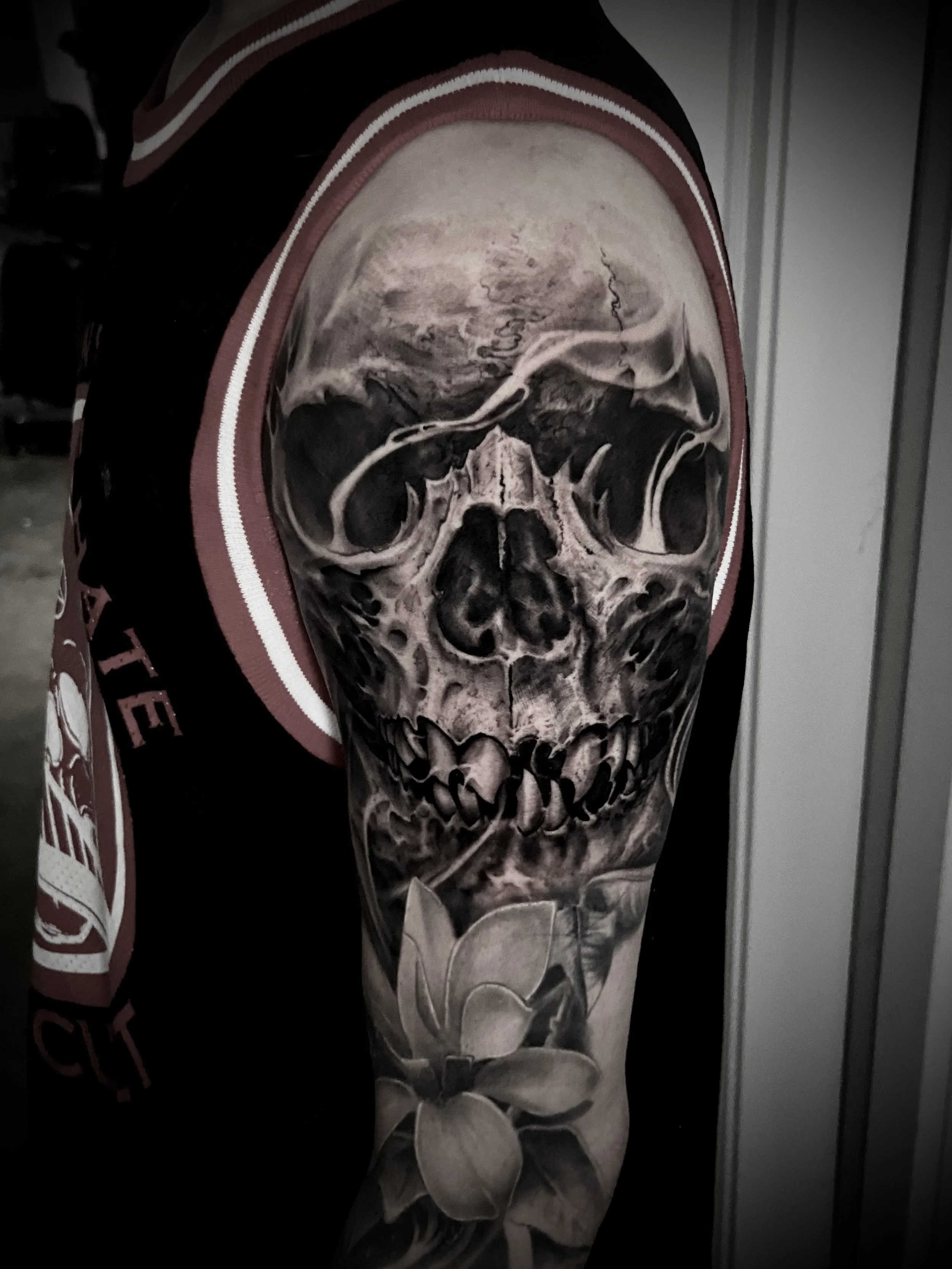 A tattoo of a realistic skull with shading and a floral design on the forearm.