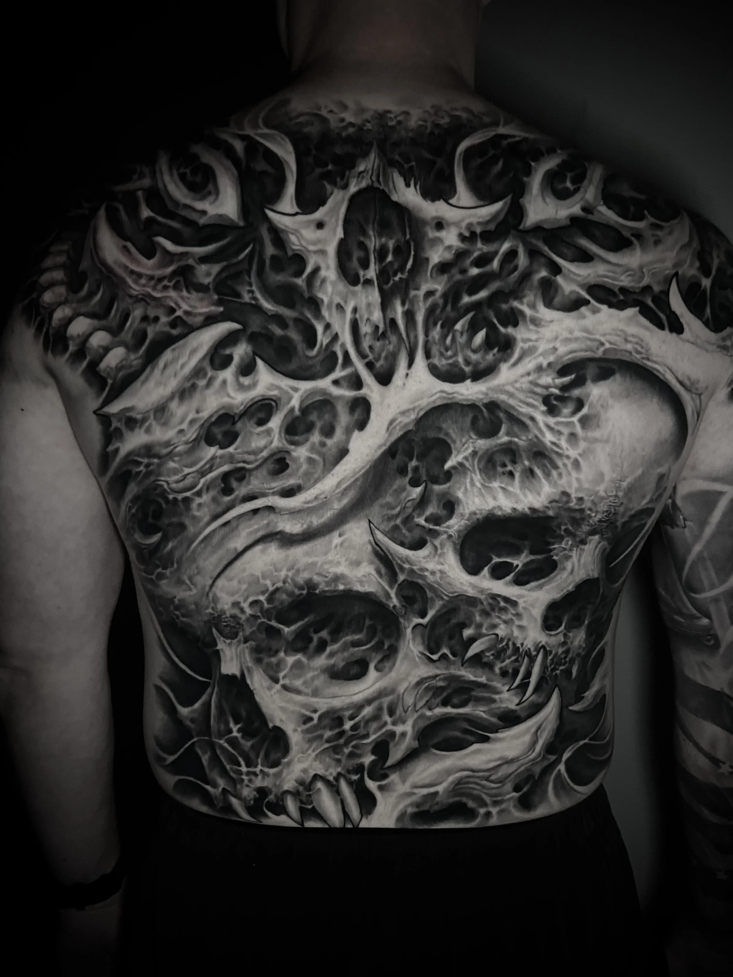 Black and white tattoo of a skull with intricate designs covering the person's back.