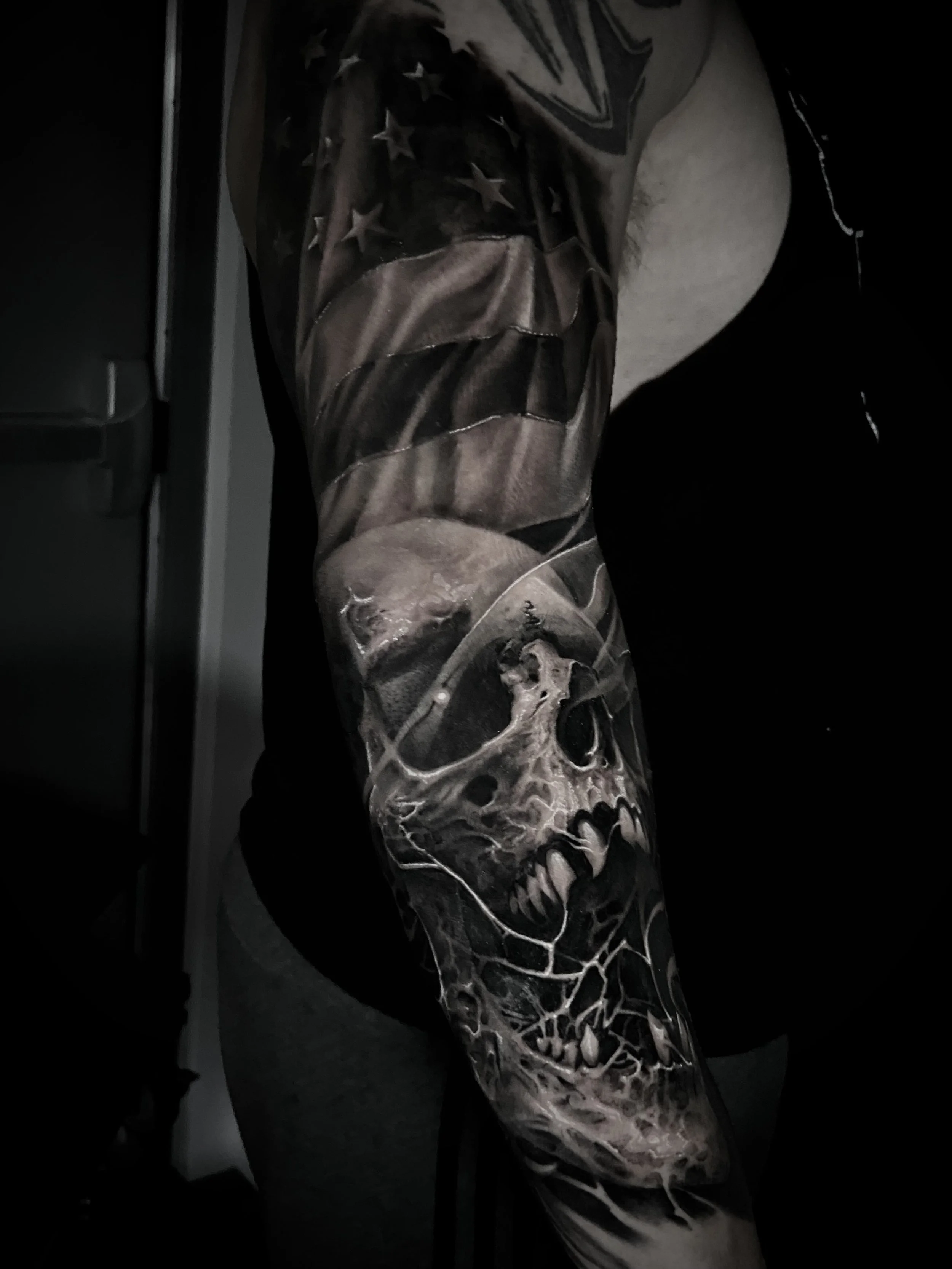 Close-up of a person's arm tattoo featuring a realistic skull with fierce teeth and hollow eyes, surrounded by abstract shading and details.