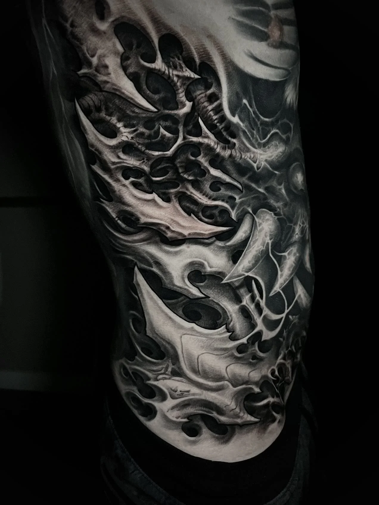 Black and gray abstract tattoo design on a person's arm, featuring swirling, smoke-like patterns and bold shapes.