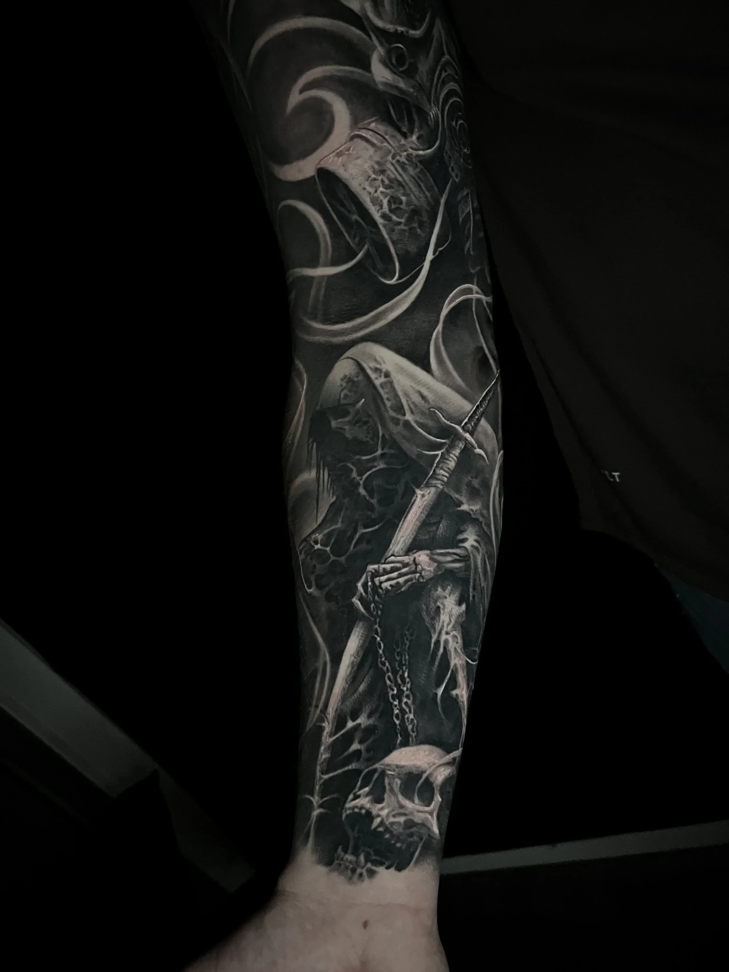 Black and gray tattoo sleeve featuring a skull, a scythe, a skeleton, and various dark, smoky details.