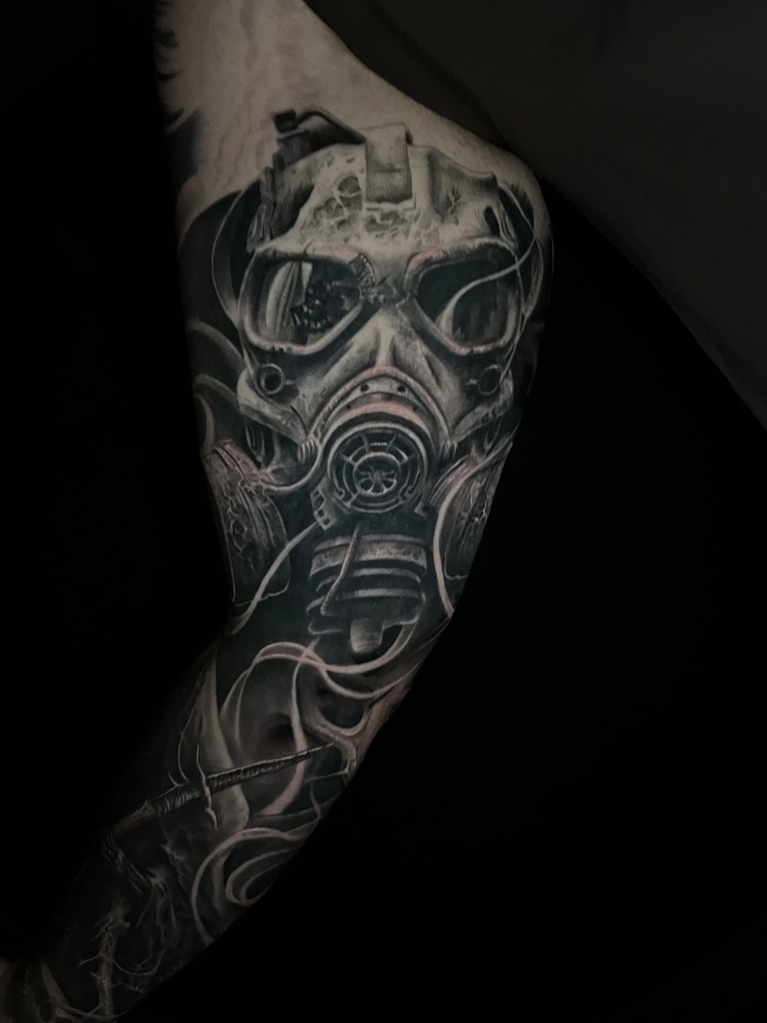 A black and gray tattoo of a futuristic gas mask with detailed shading covering a person's upper arm.