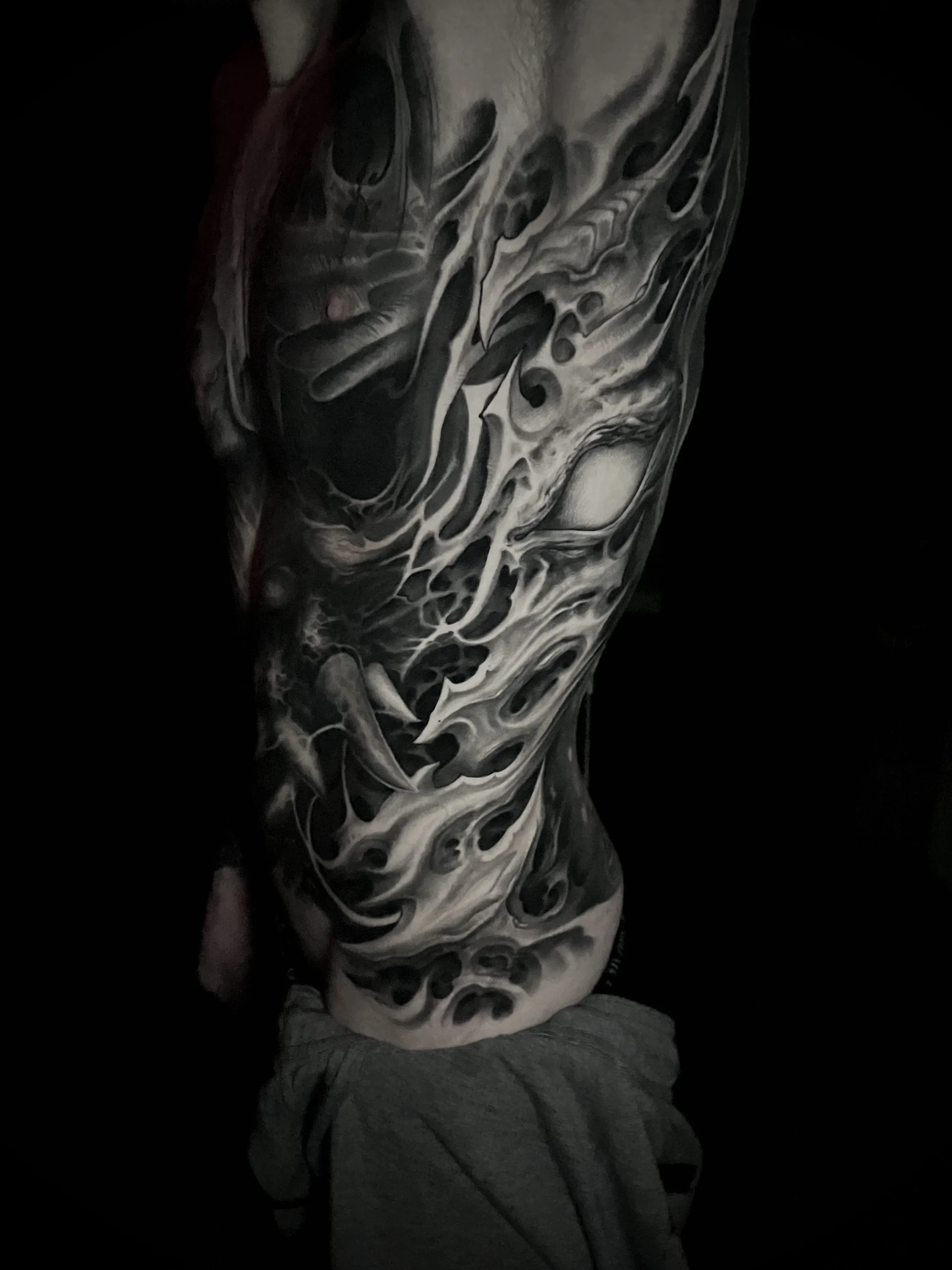 Black and white abstract tattoo covering an arm and shoulder, with swirling and flowing patterns.