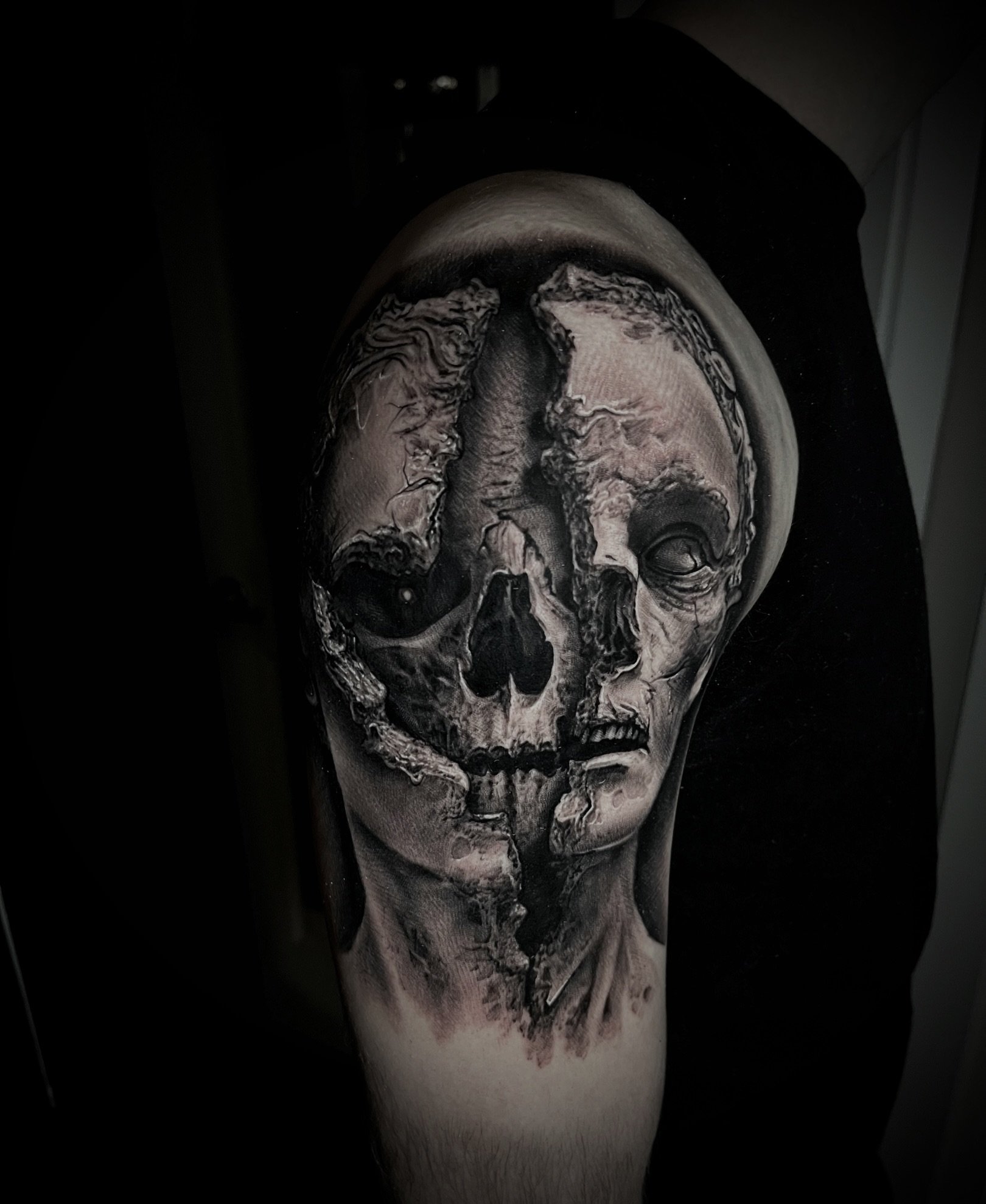 Tattoo of a face with half human and half skull design on a person's arm.
