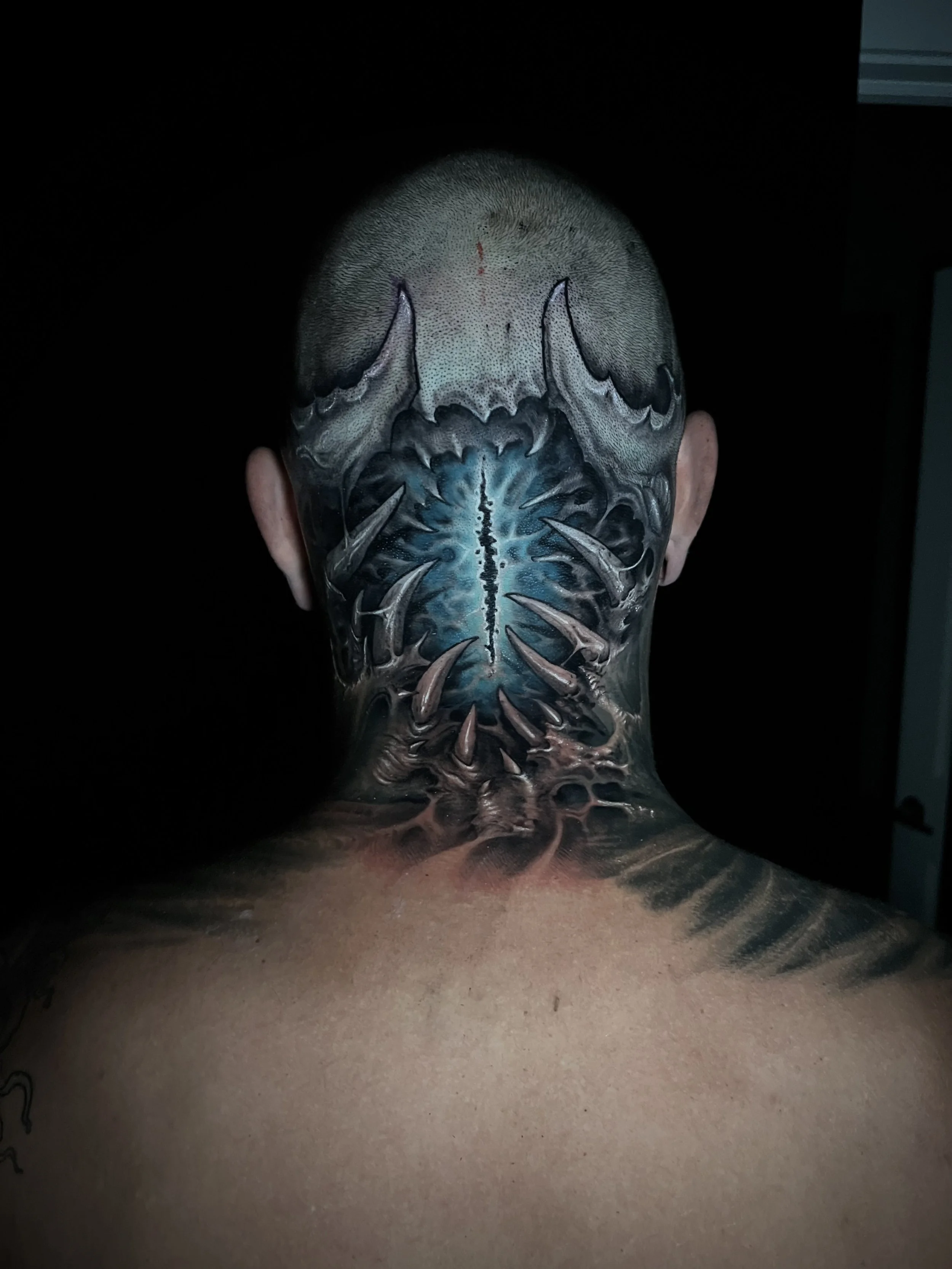 Back tattoo of a fierce creature with sharp teeth and claws, in blue, black, and gray shades.