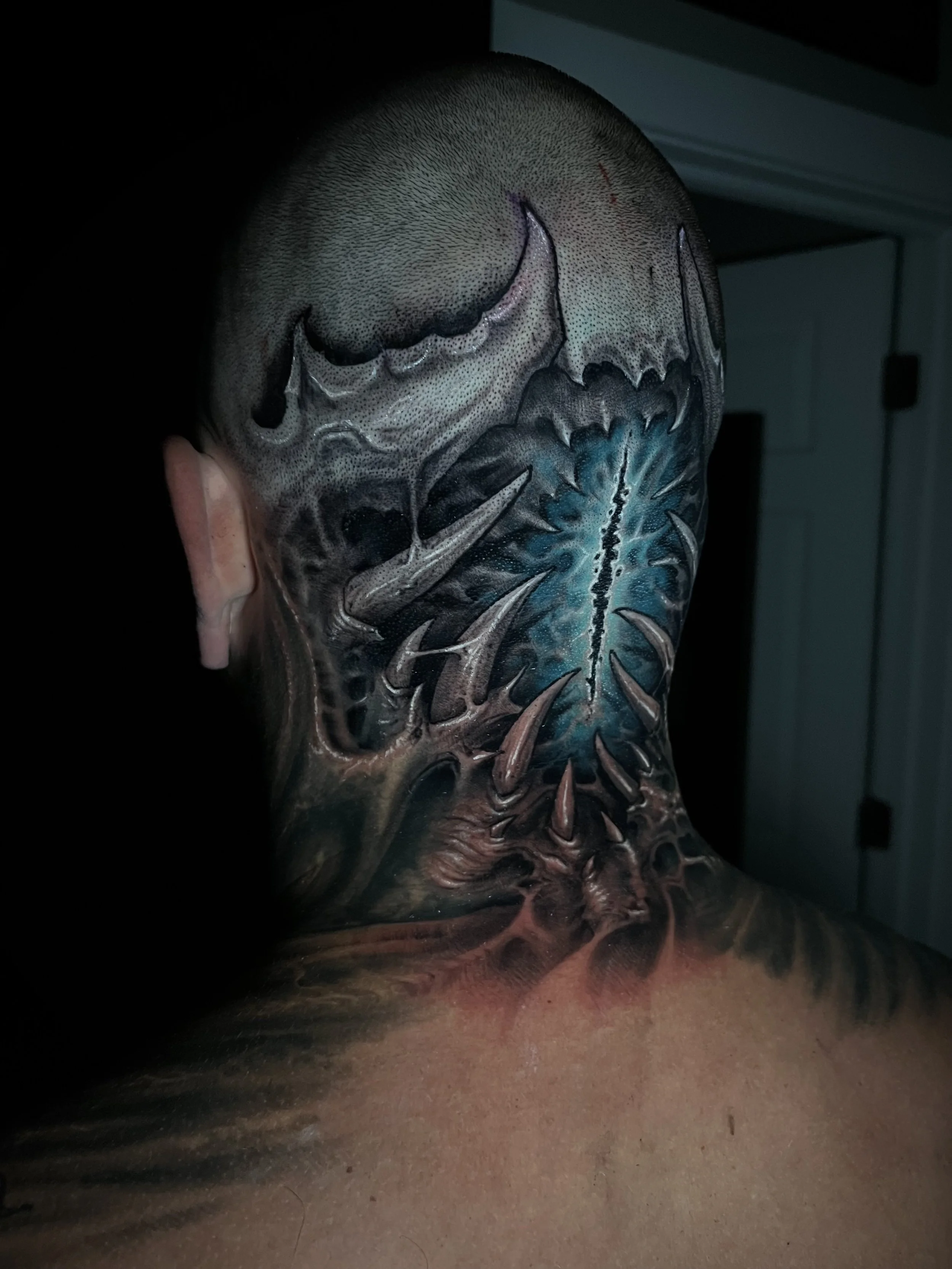 Back of a person's head and neck with a detailed, colorful tattoo featuring a skull, spikes, and a blue energy center.