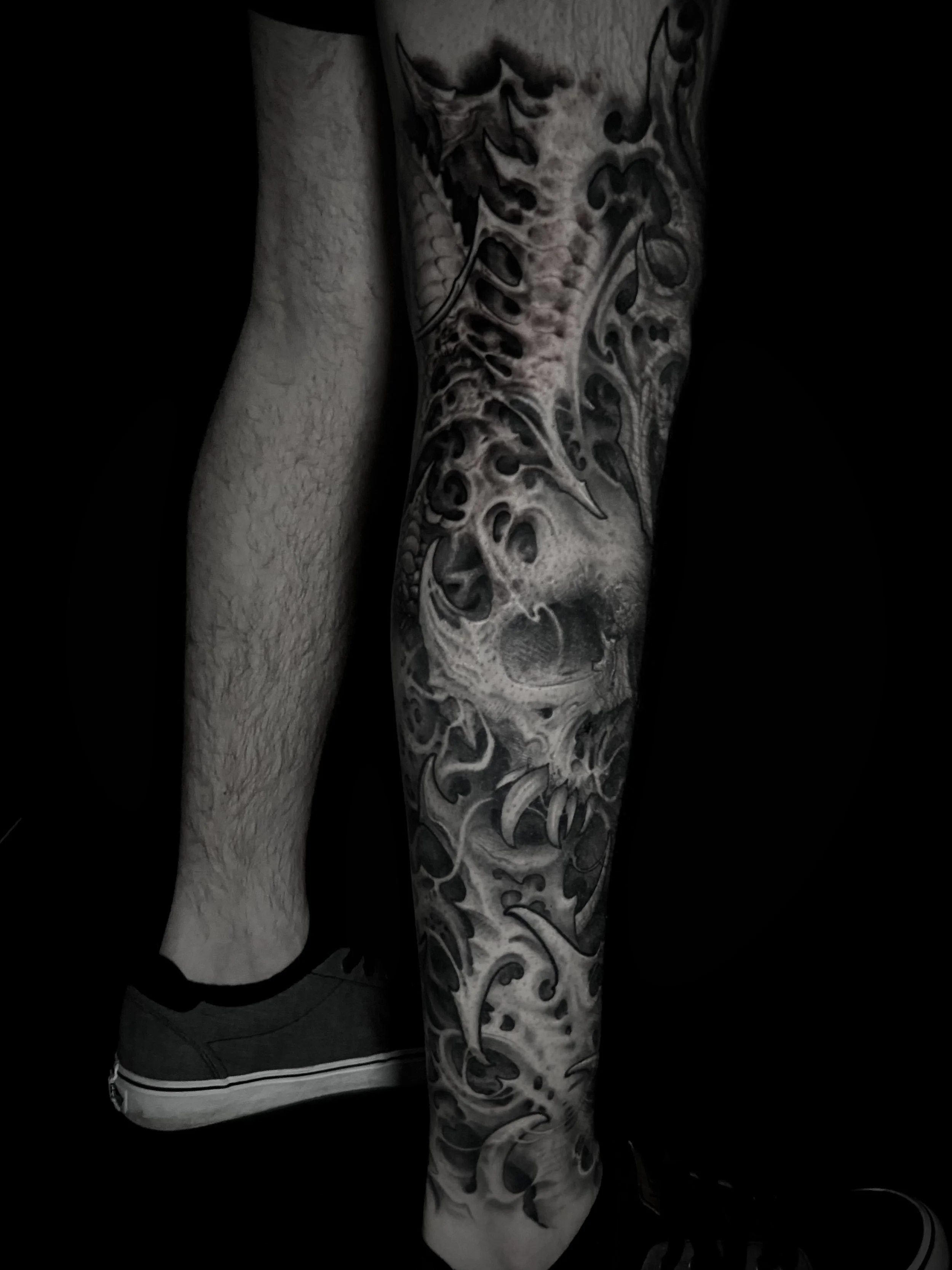 A person with a detailed black and gray tattoo sleeve of a skull and abstract designs on their leg.