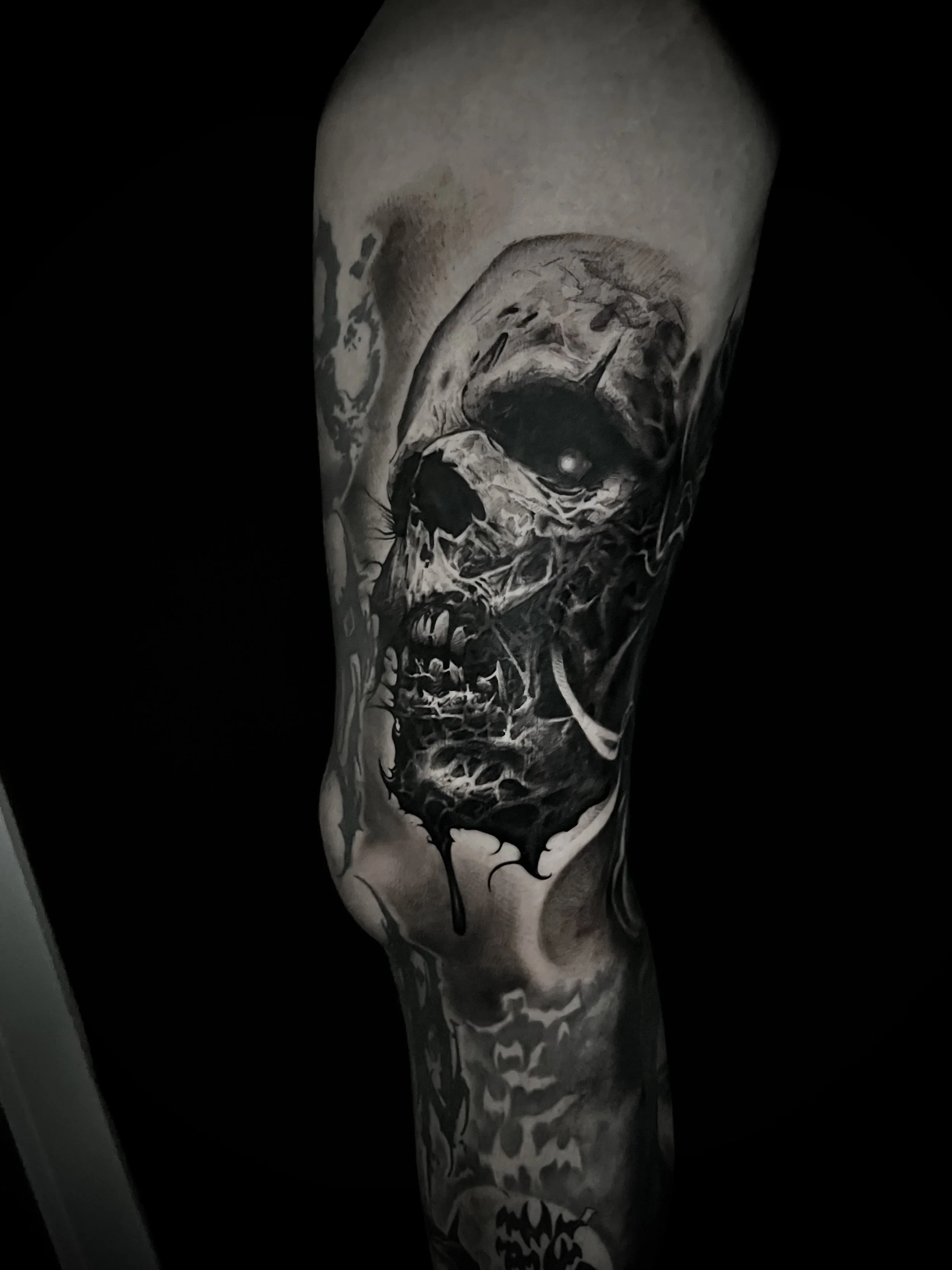 Black and gray tattoo of a skull with a raven perched on it, with dripping ink effects.