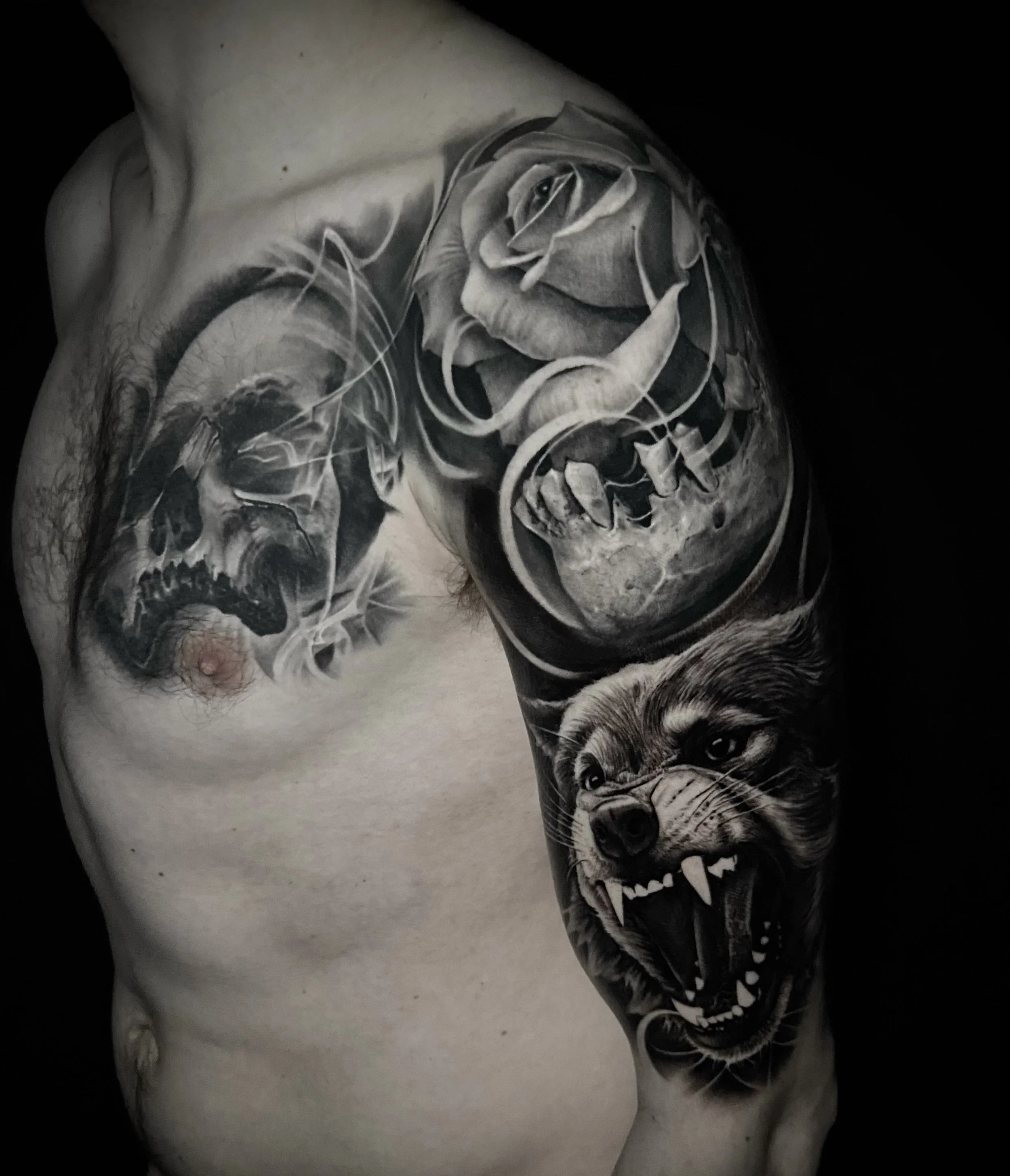 Black and gray tattoo sleeve featuring a rose, a snarling wolf, a skull, and a distorted face.