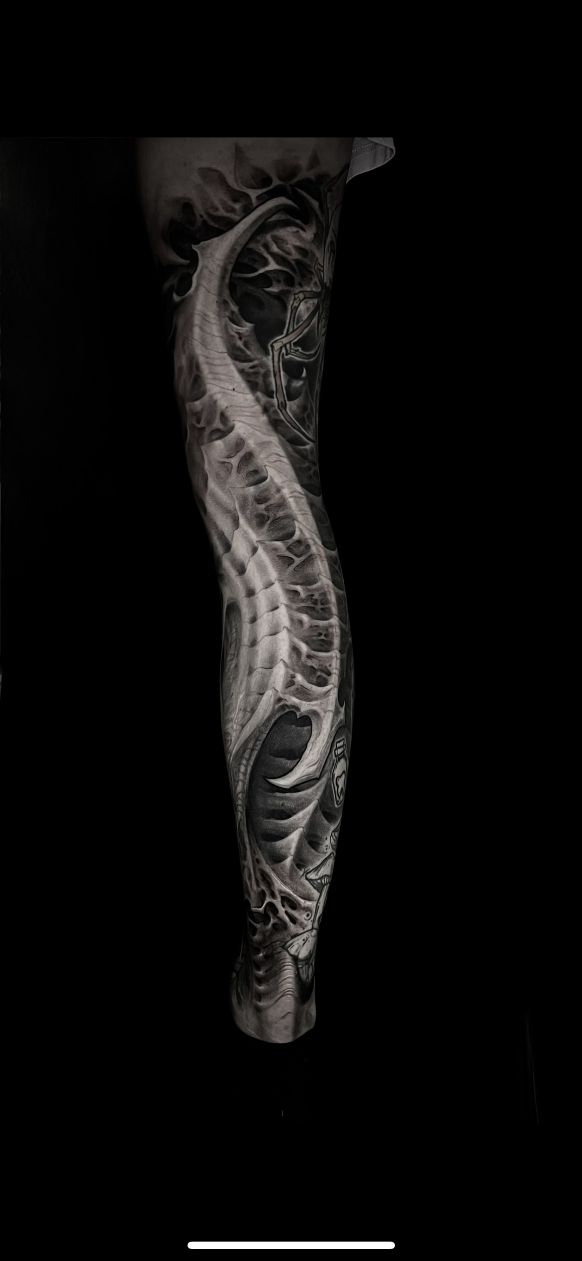 Black and gray tattoo sleeve featuring a detailed skeleton and skull design on a person's arm against a black background.