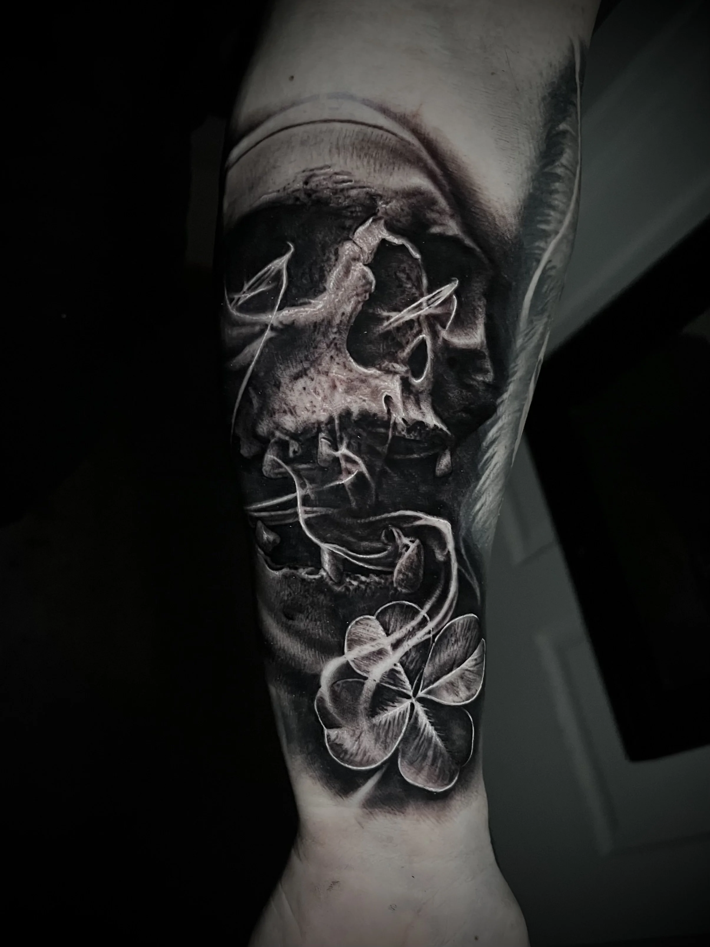 A black and gray tattoo of a human skull with abstract and floral elements on a person's arm.