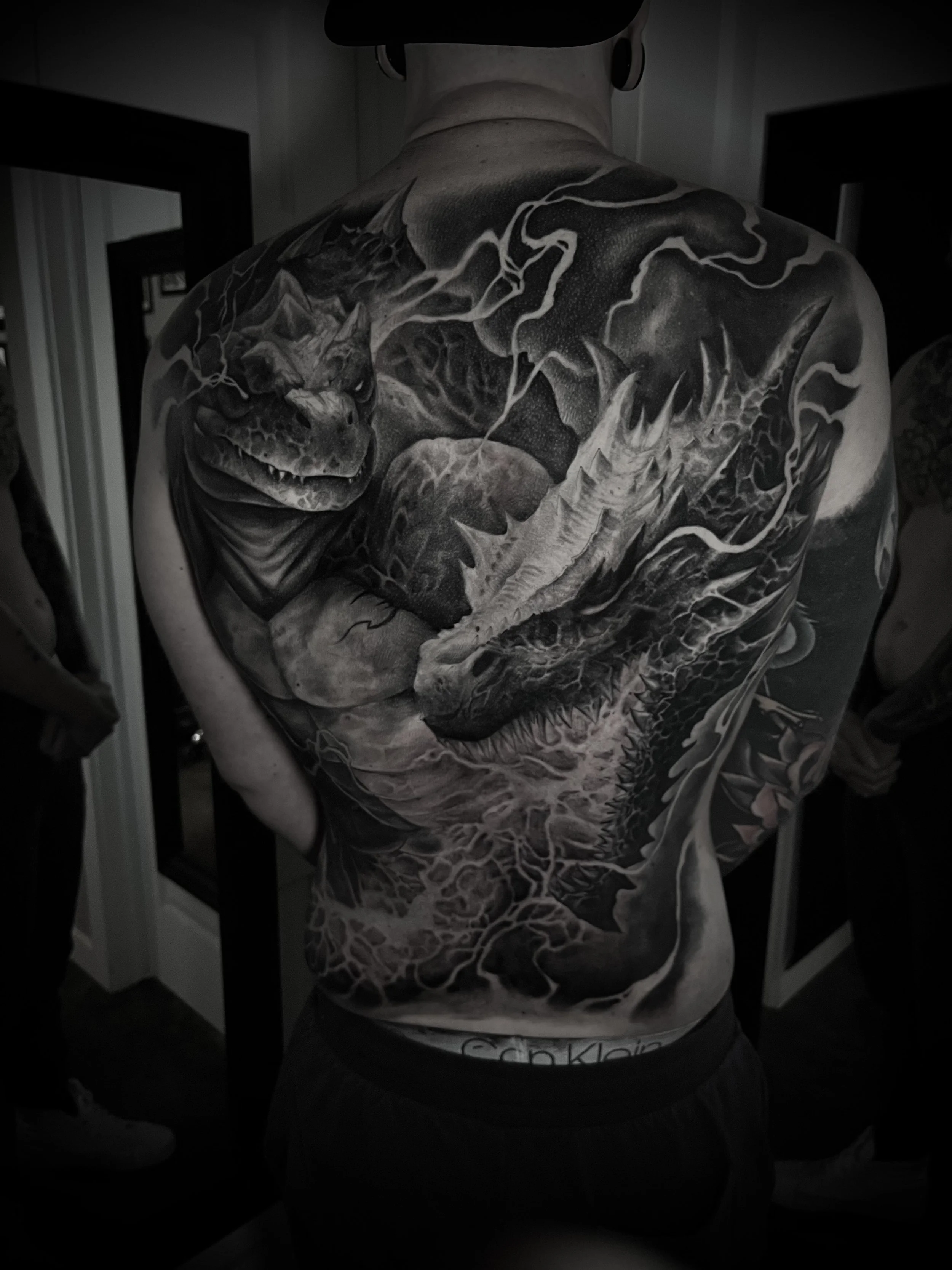 Black and gray tattoo of a dragon and a dinosaur on a person's back