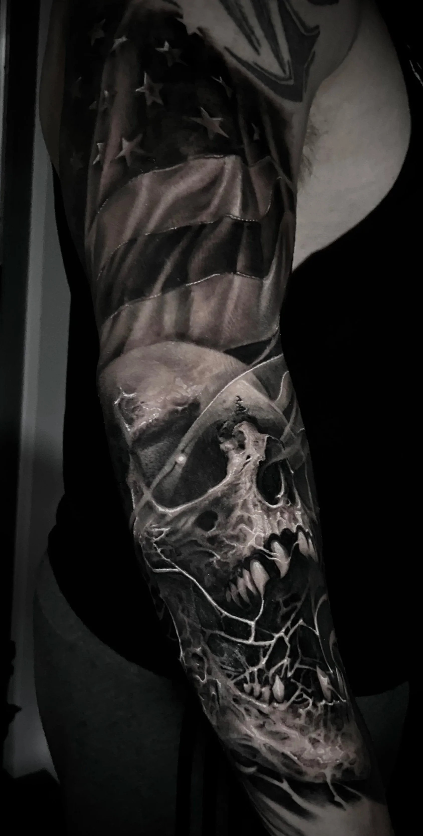 A black and gray tattoo sleeve featuring a realistic human skull and abstract patterns.