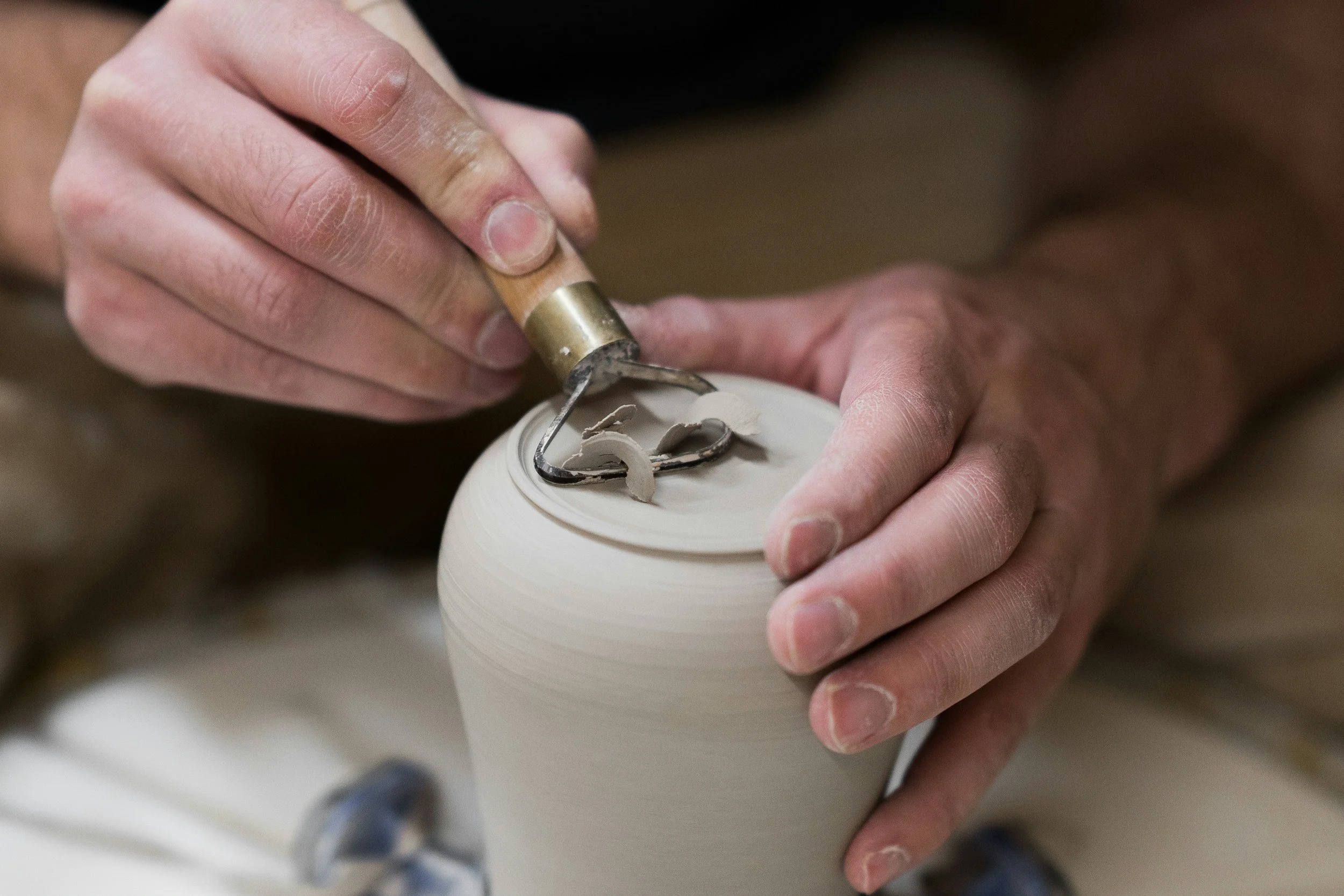 Close-up of a person carving a design into a ceramic vase with a metal carving tool.