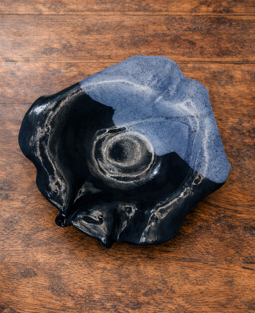 A decorative blue flower ceramic bowl with a wavy, ruffled edge, black on the outside and blue on the inside on wooden surface.