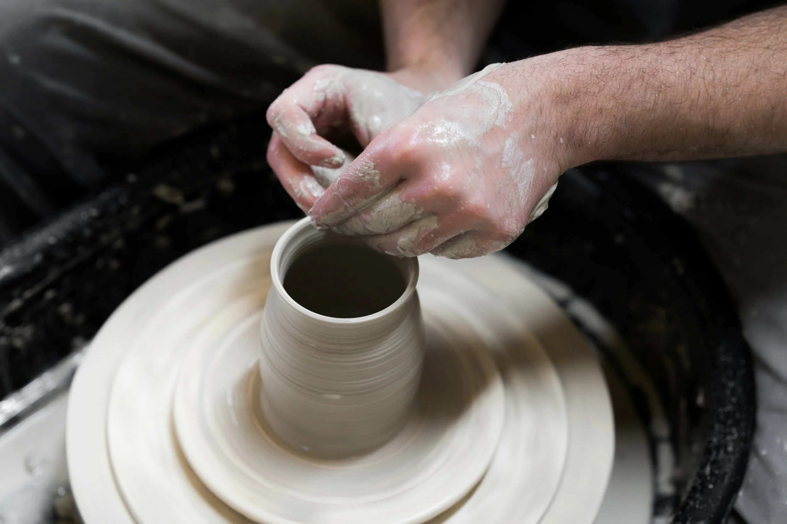 A person shaping a ceramic vase on a pottery wheel, hands covered in clay.