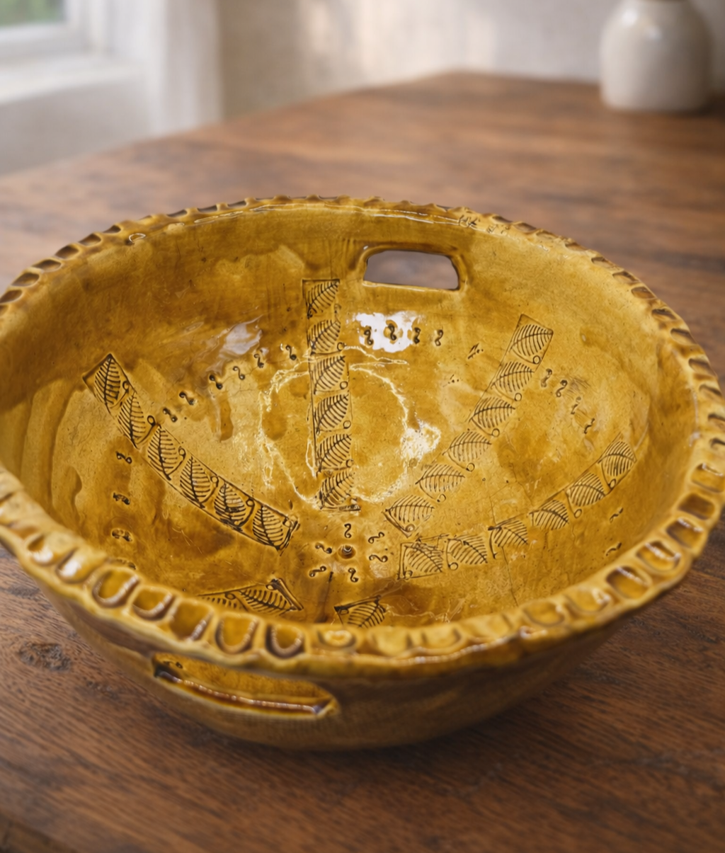 A yellow pottery bowl with geometric patterns on the inside, sitting on a wooden table.