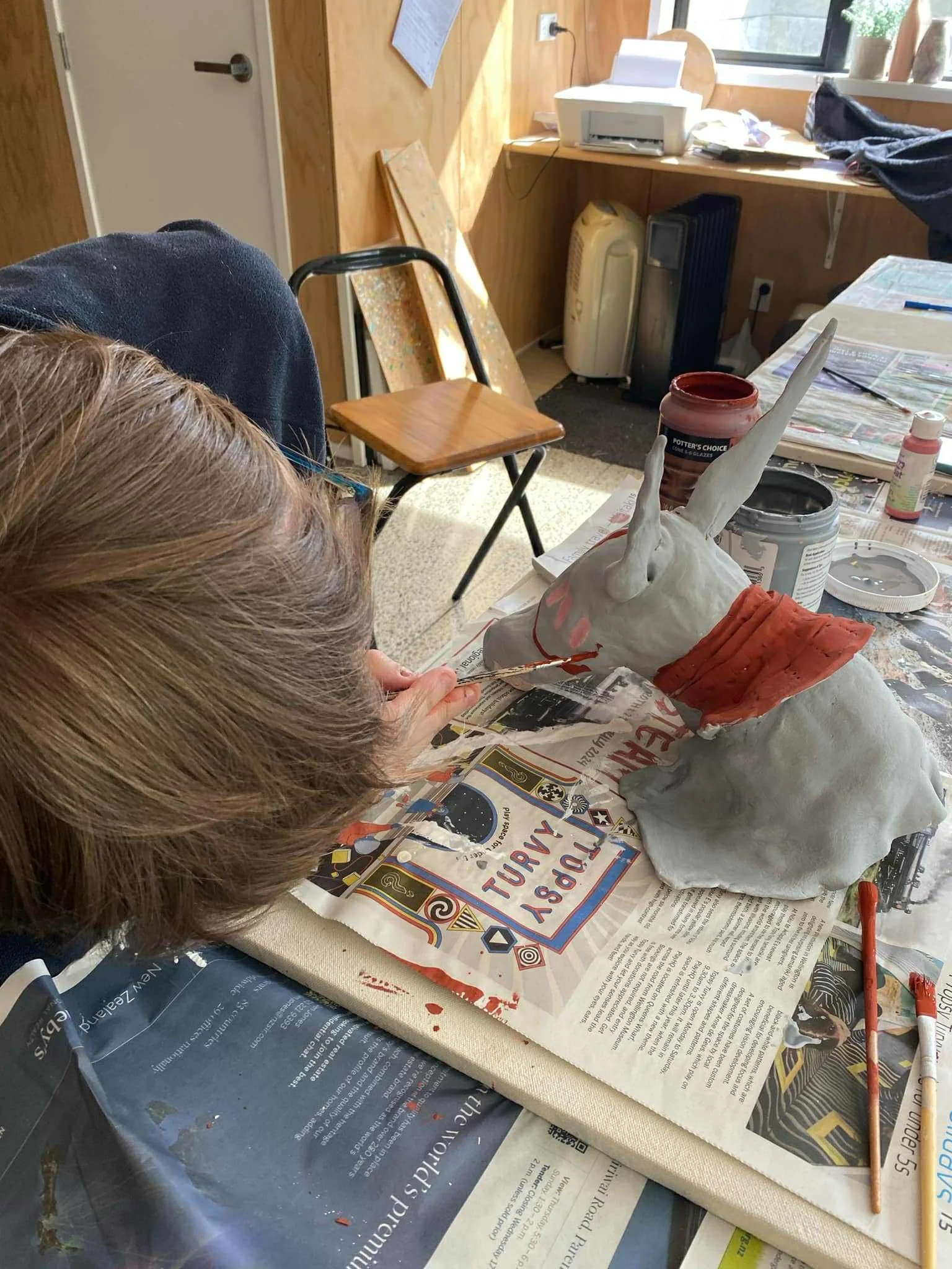 Louis painting a unicorn sculpture with red paint at a cluttered workspace.