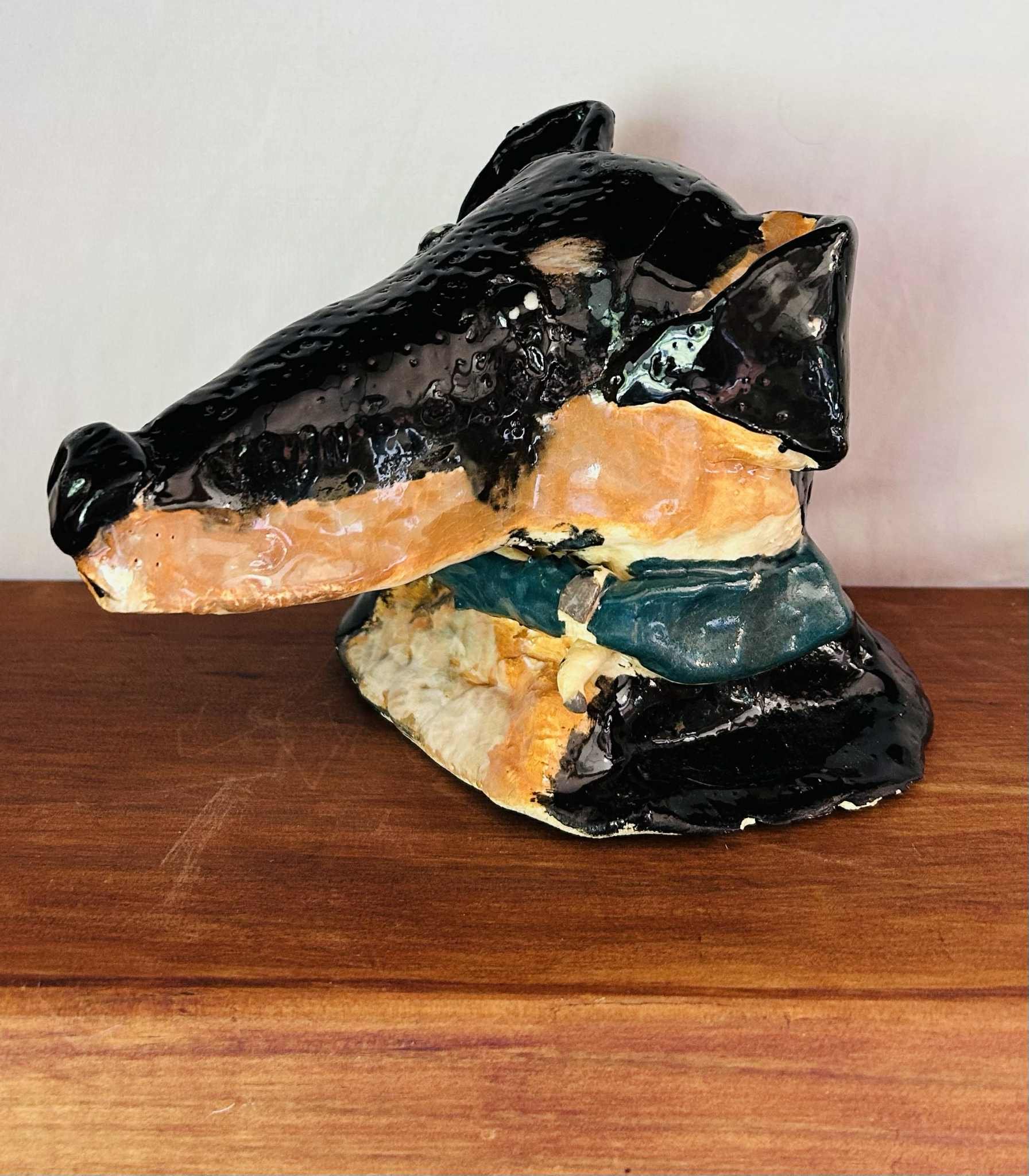 Ceramic sculpture of a dog's head resting on a wooden surface.
