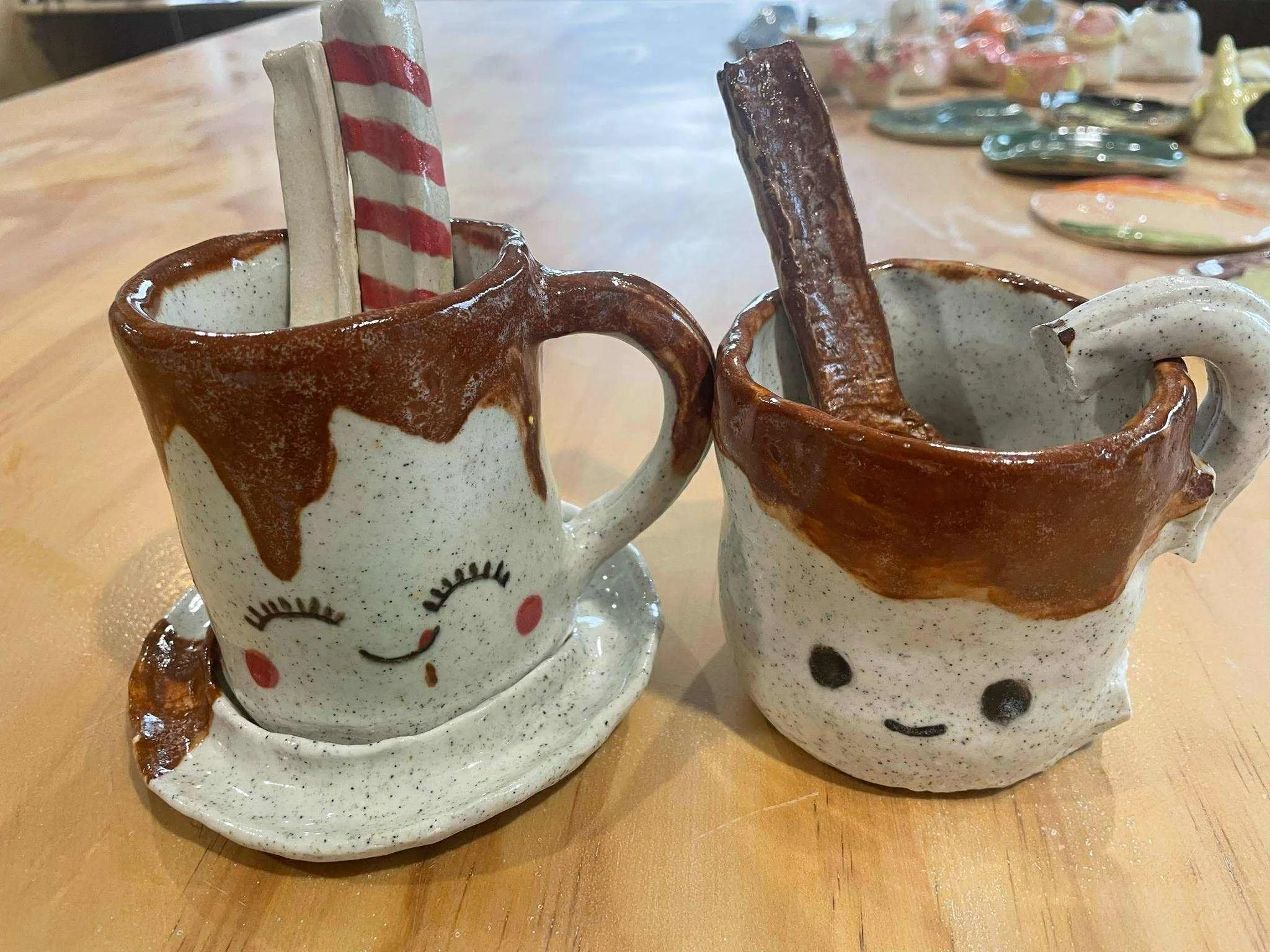 Two ceramic mugs with smiling faces and closed eyes placed on a wooden table.