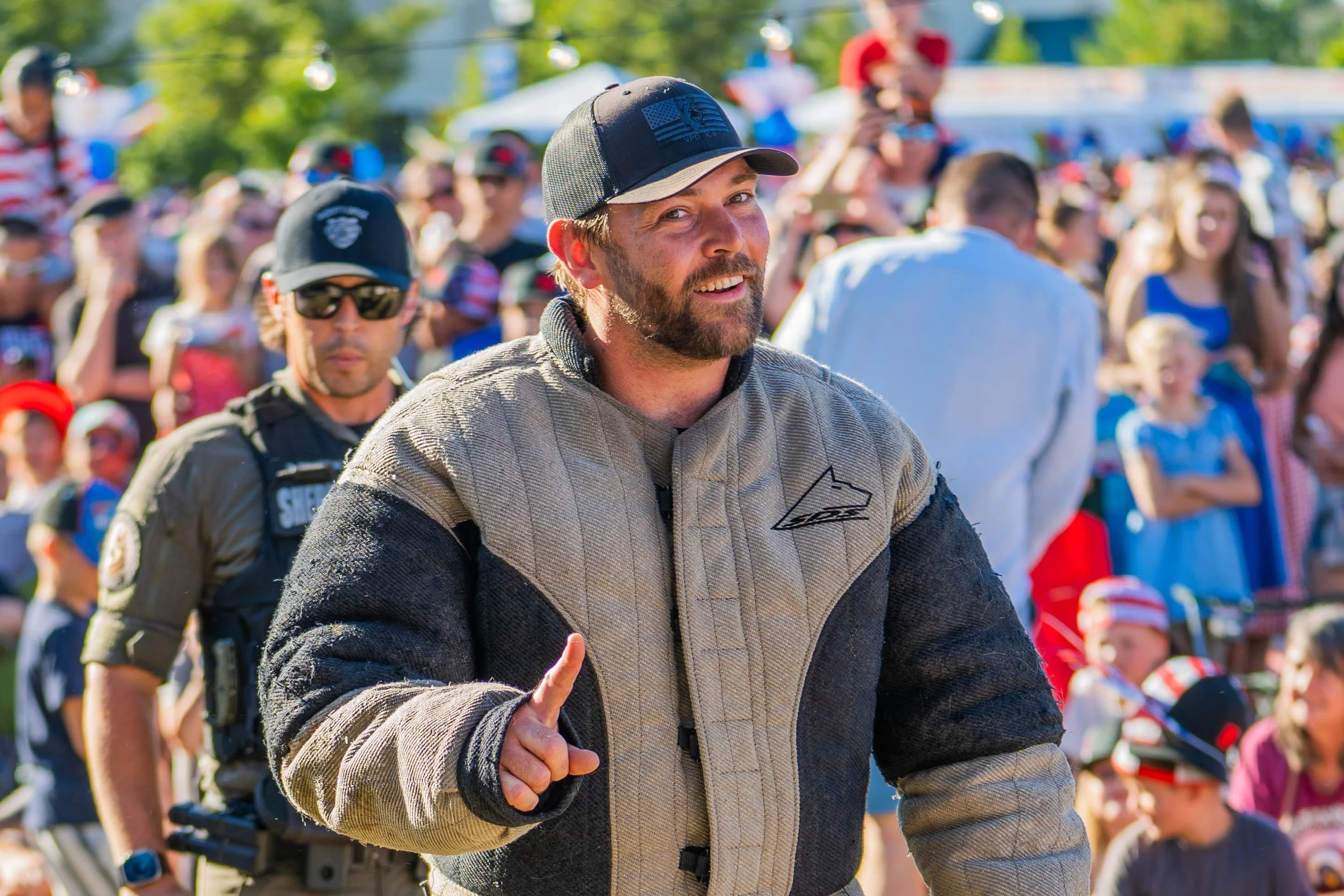 A man in a motorcycle racing jacket and cap running outdoors with a large crowd of spectators in the background.