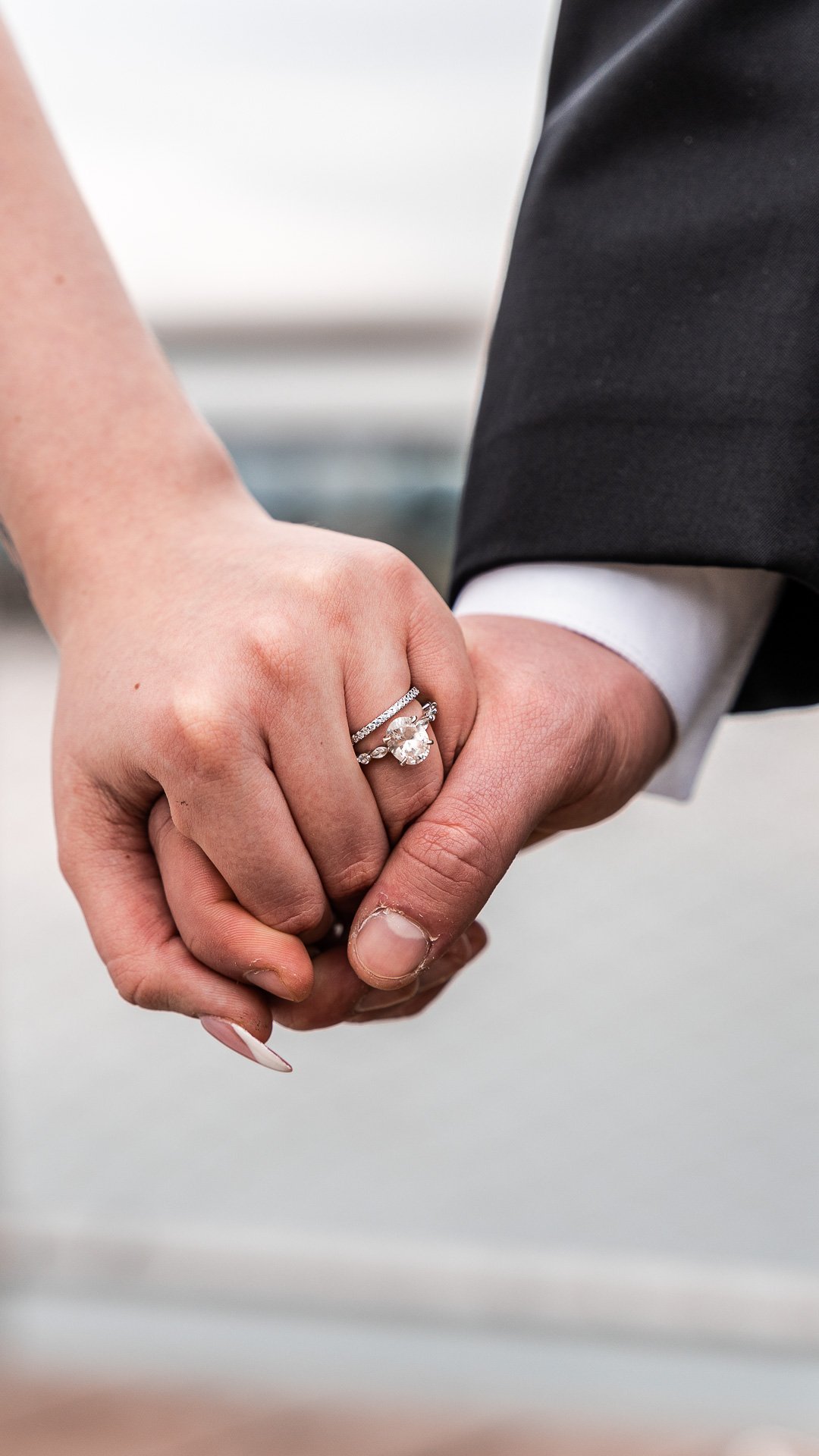 Close-up of a couple holding hands, showcasing wedding and engagement rings.