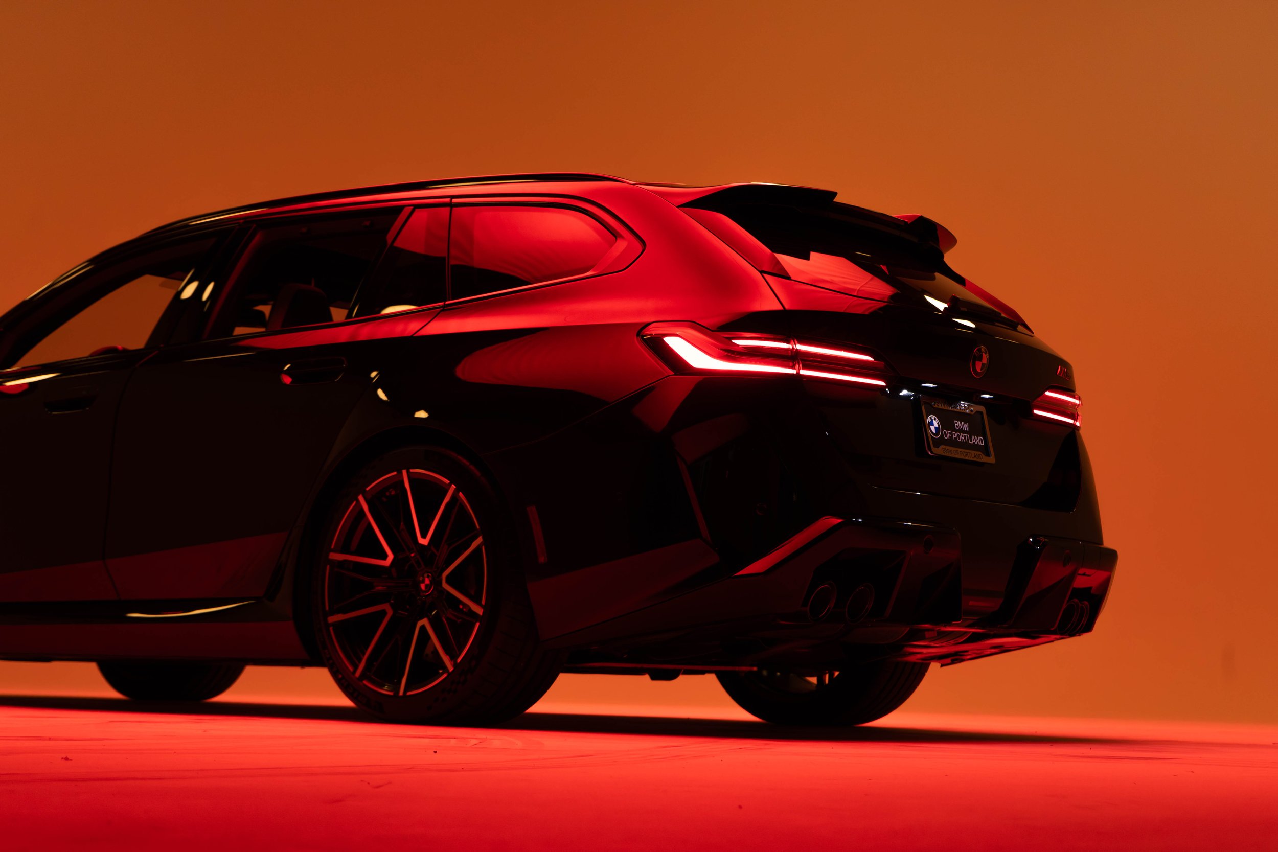 A sleek, black BMW car with red accents and illuminated taillights is shown in a dark setting with an orange background.